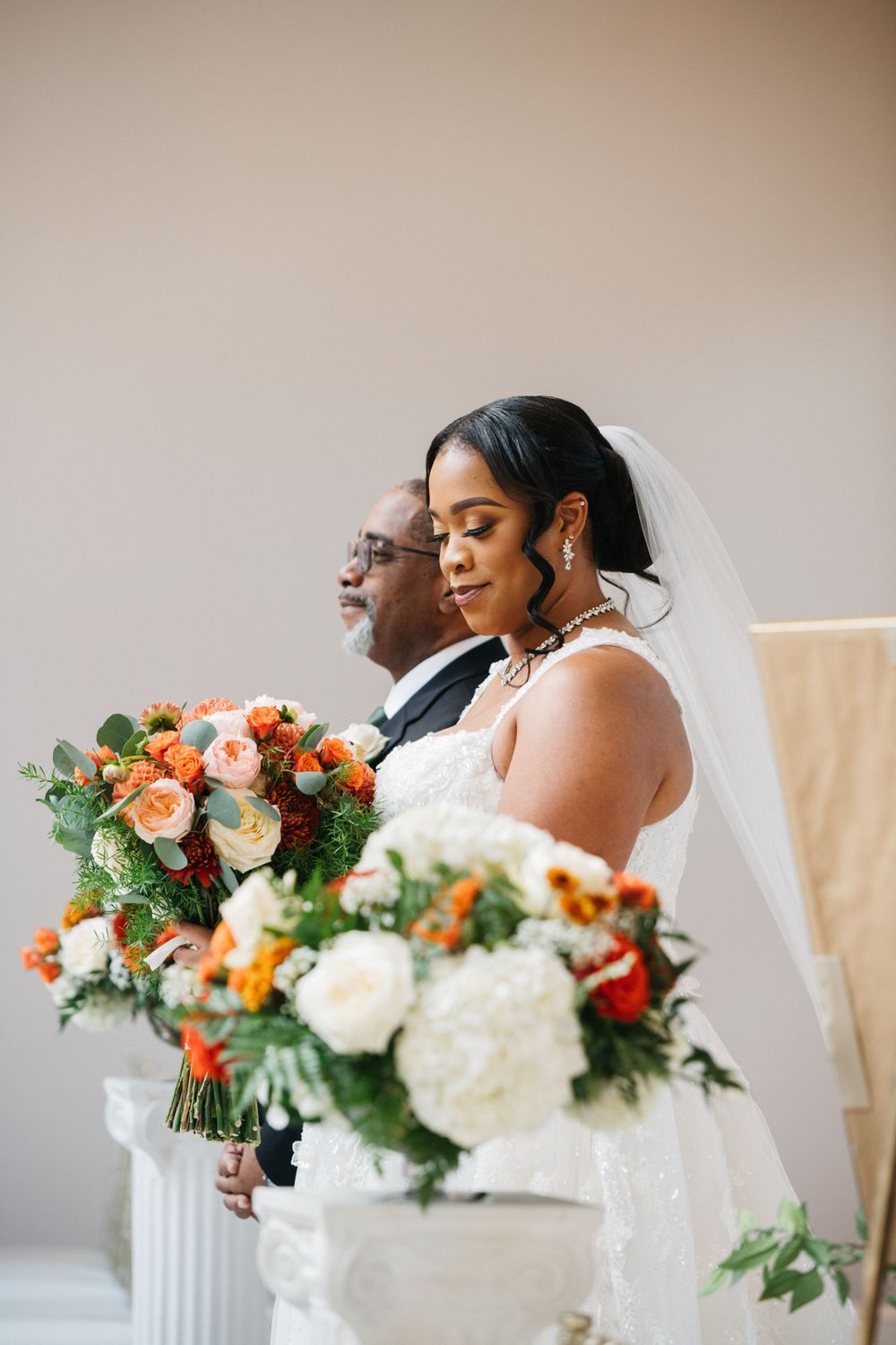 Beautiful bride holds a lush bouquet of white and orange flowers while standing next to someone special.