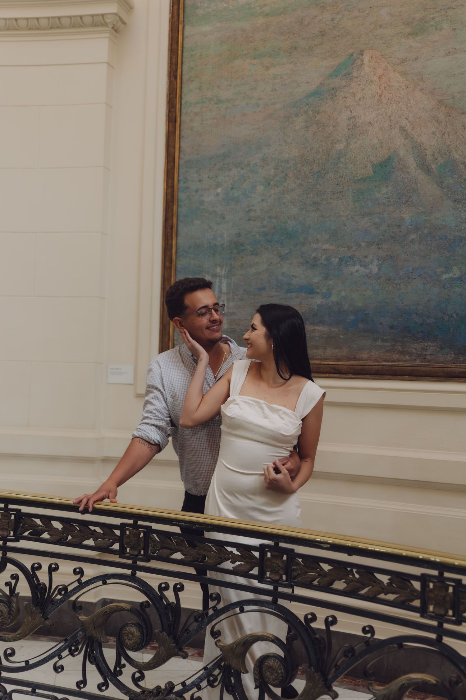 Couple sharing a tender moment on an elegant staircase beside a large mountain painting.