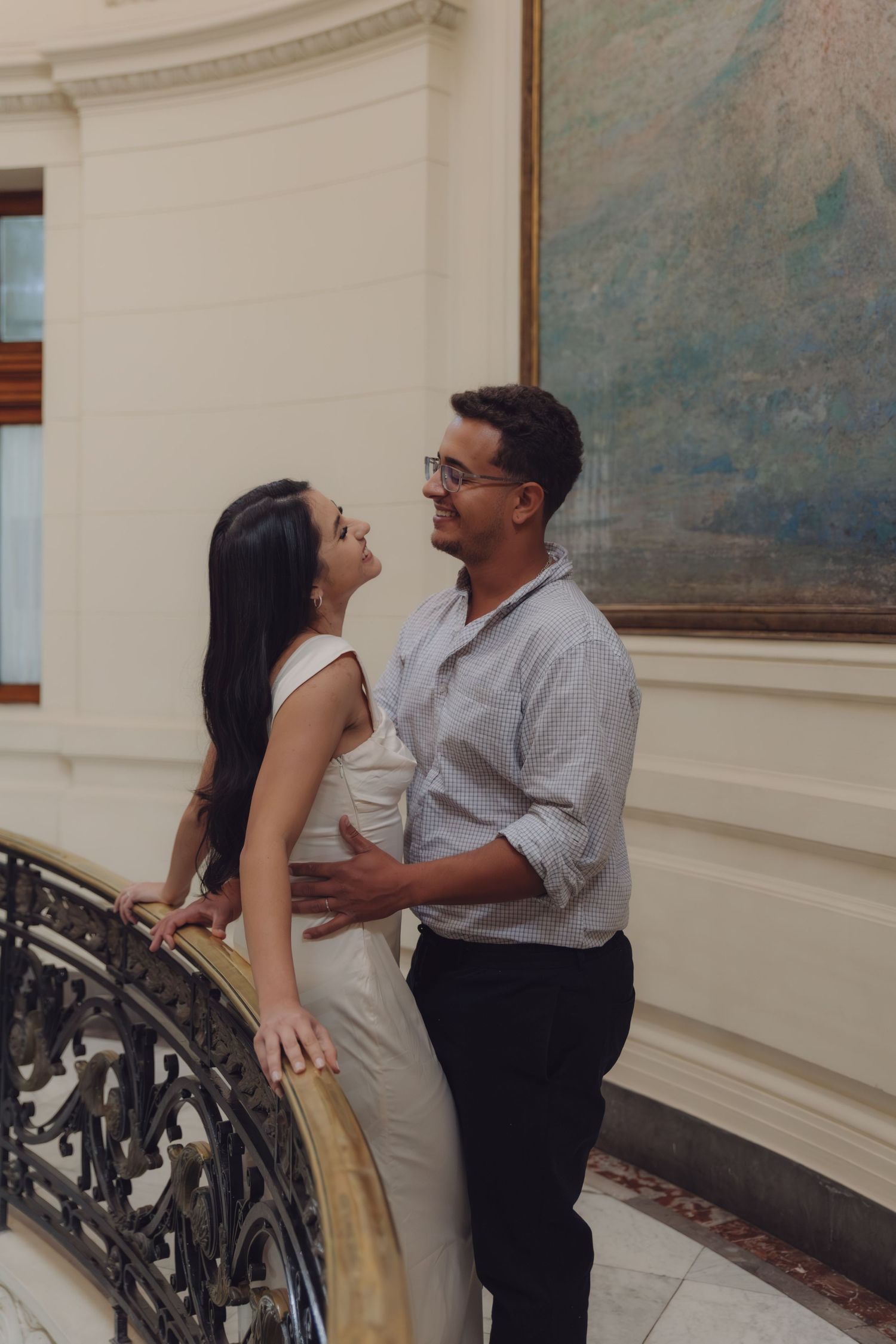 Couple embracing and smiling at each other on an ornate staircase in a grand building.