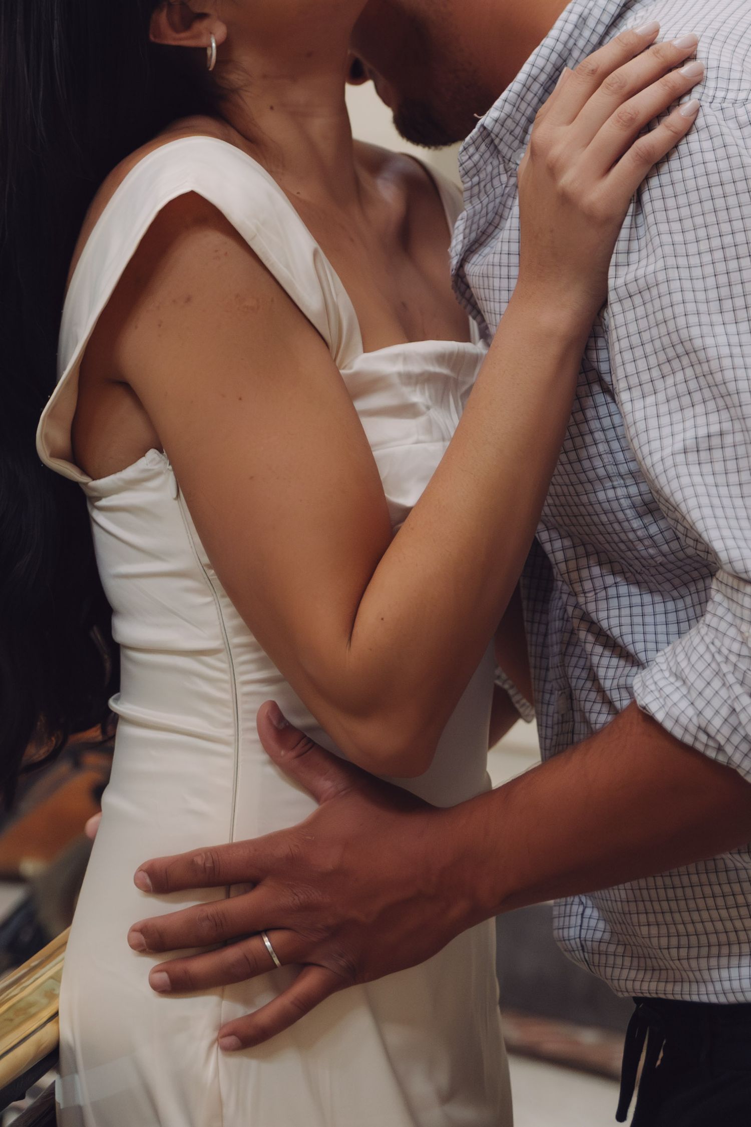 A couple in an intimate embrace, the woman in a white dress and man in a plaid shirt, sharing a tender moment.
