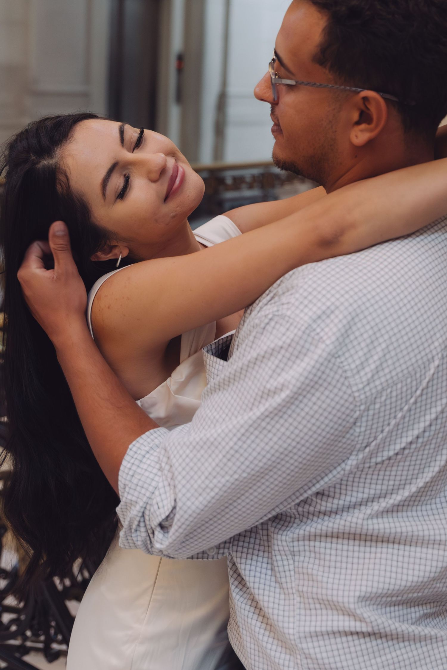 A man gently strokes a woman's hair as she leans into him with closed eyes in an elegant interior.