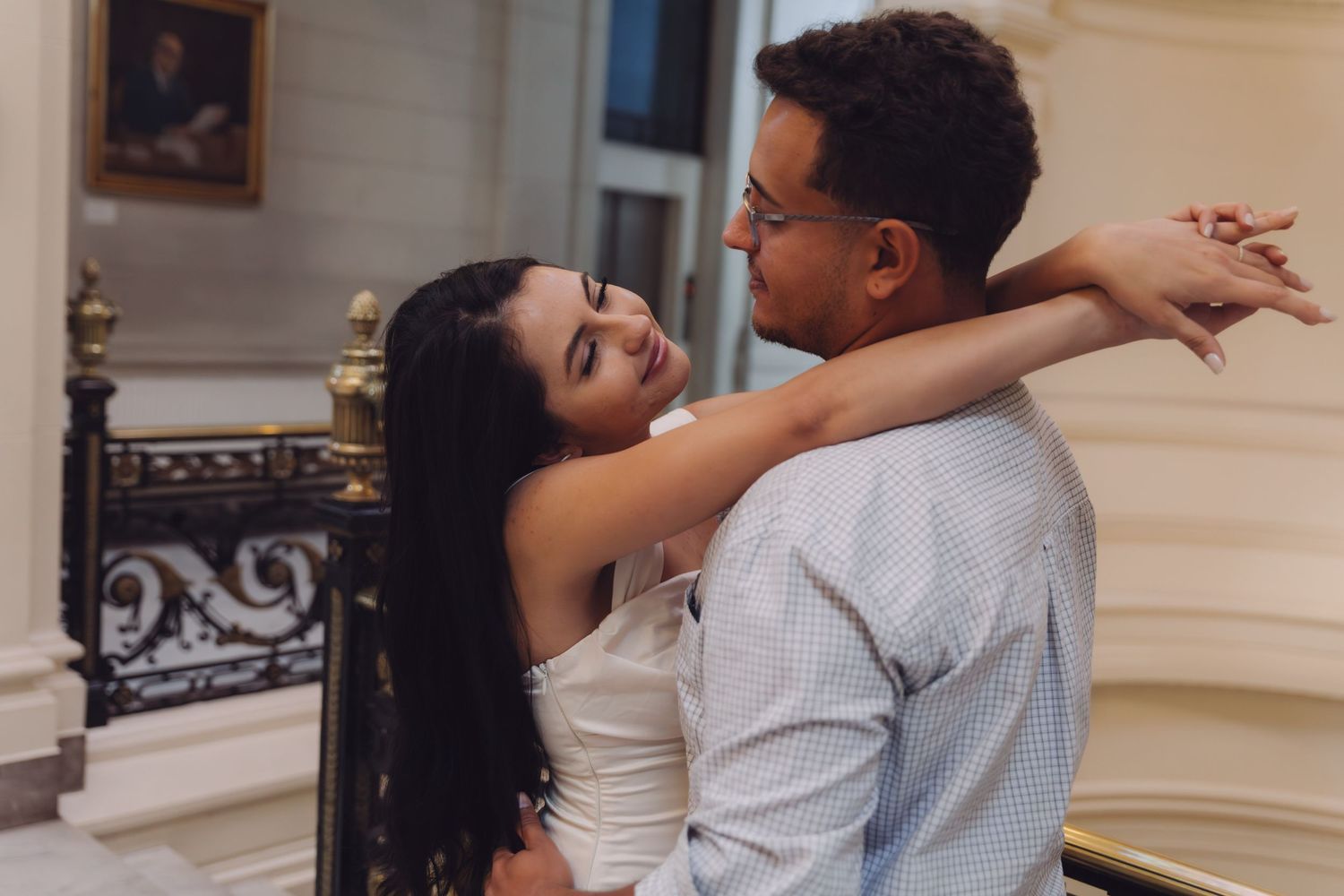 A couple shares a tender embrace on an ornate staircase, the woman smiling as she holds the man close.
