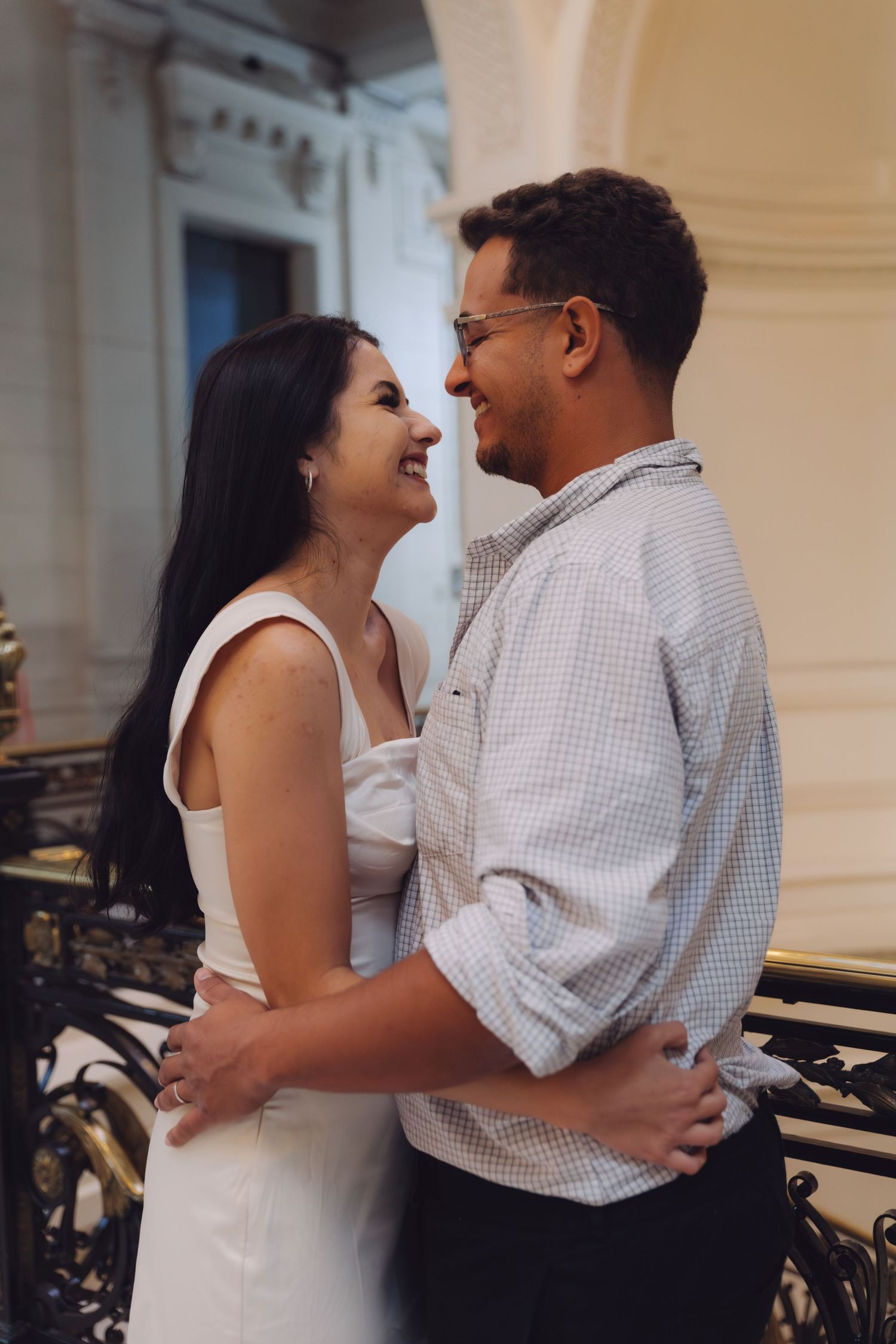 Happy couple laughing together while embracing on an ornate balcony in a grand building.