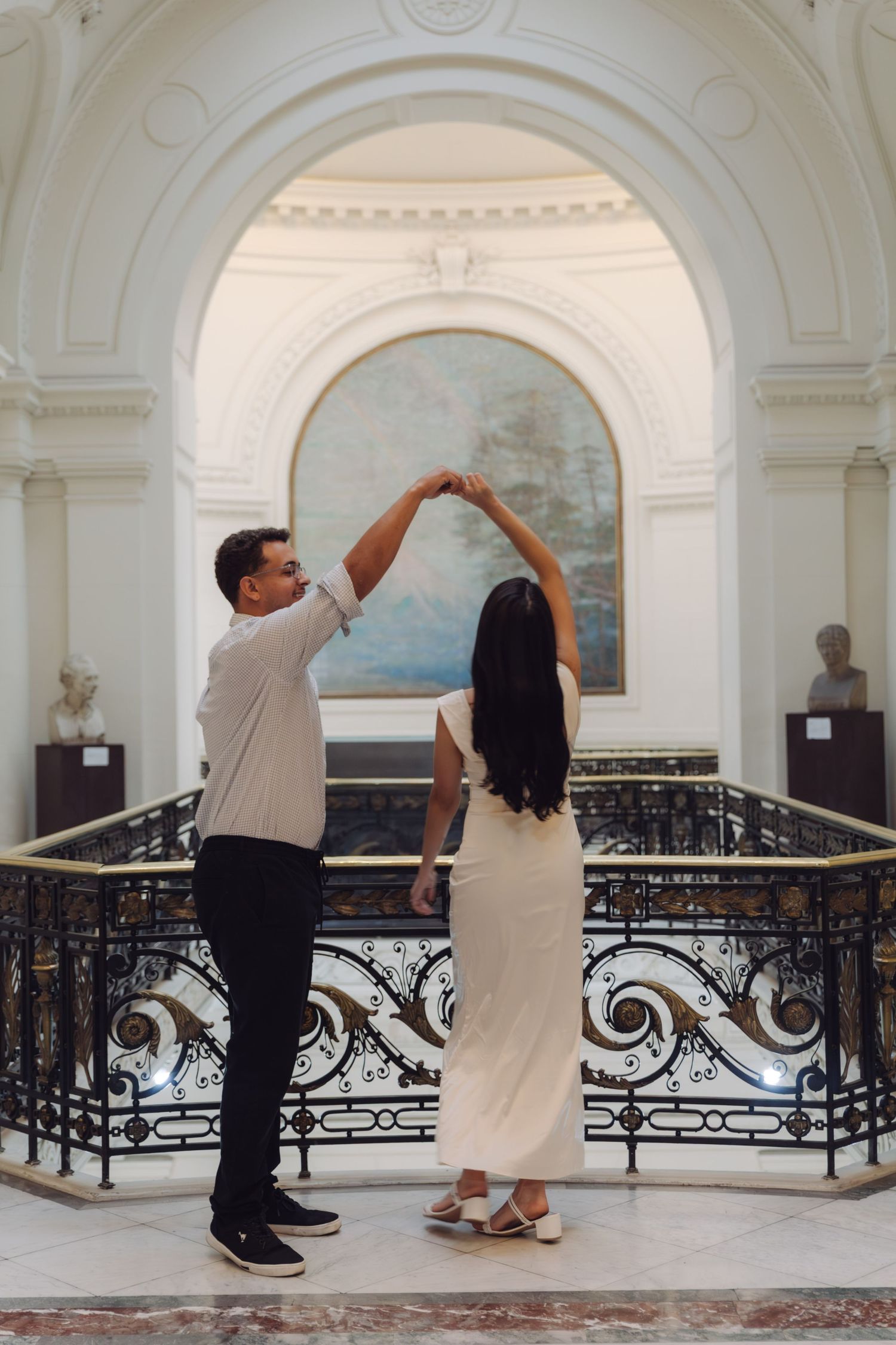 Couple dancing elegantly in a grand hall with arched decor and ornate iron railings.