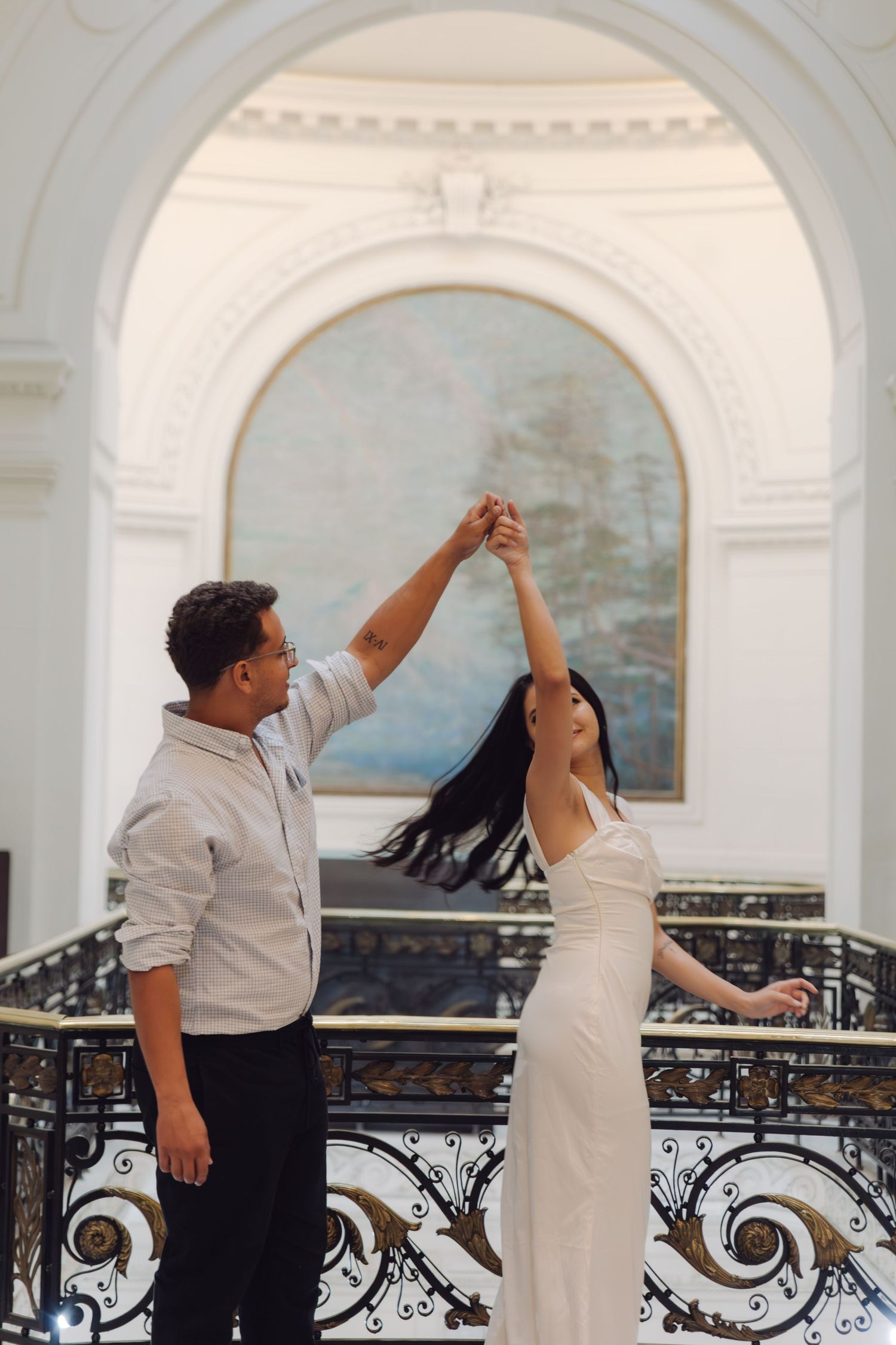 Couple spinning joyfully in a stunning white ballroom with arched painting and stained glass ceiling.