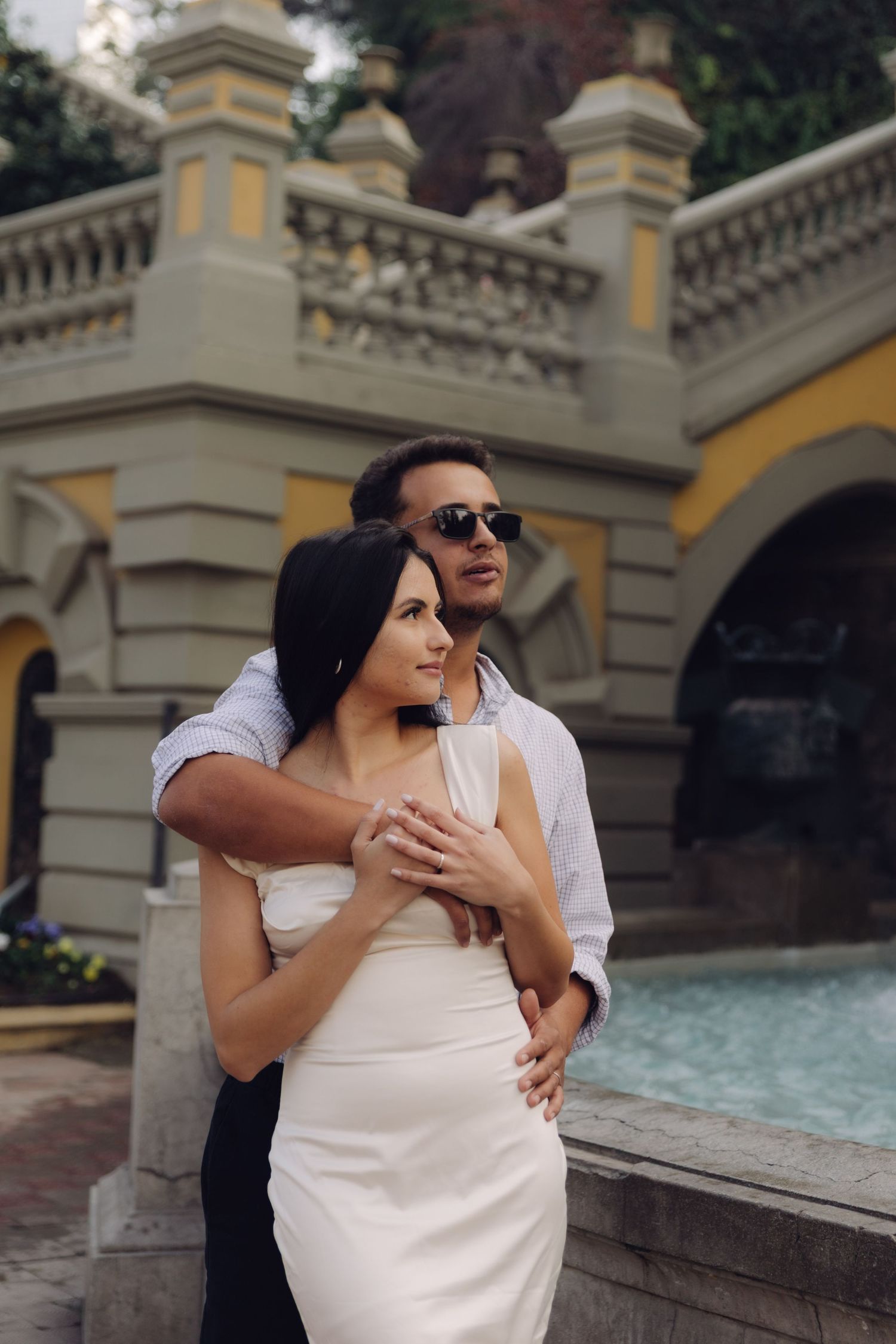 Couple embracing near a decorative fountain in an elegant yellow and white architectural setting.