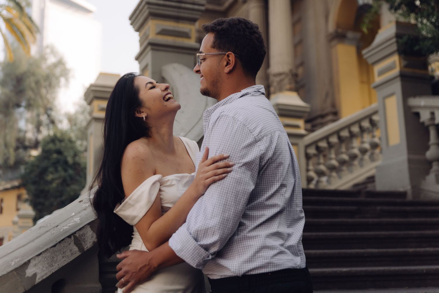 Romantic couple embracing and laughing together on ornate stone steps of a historic building.
