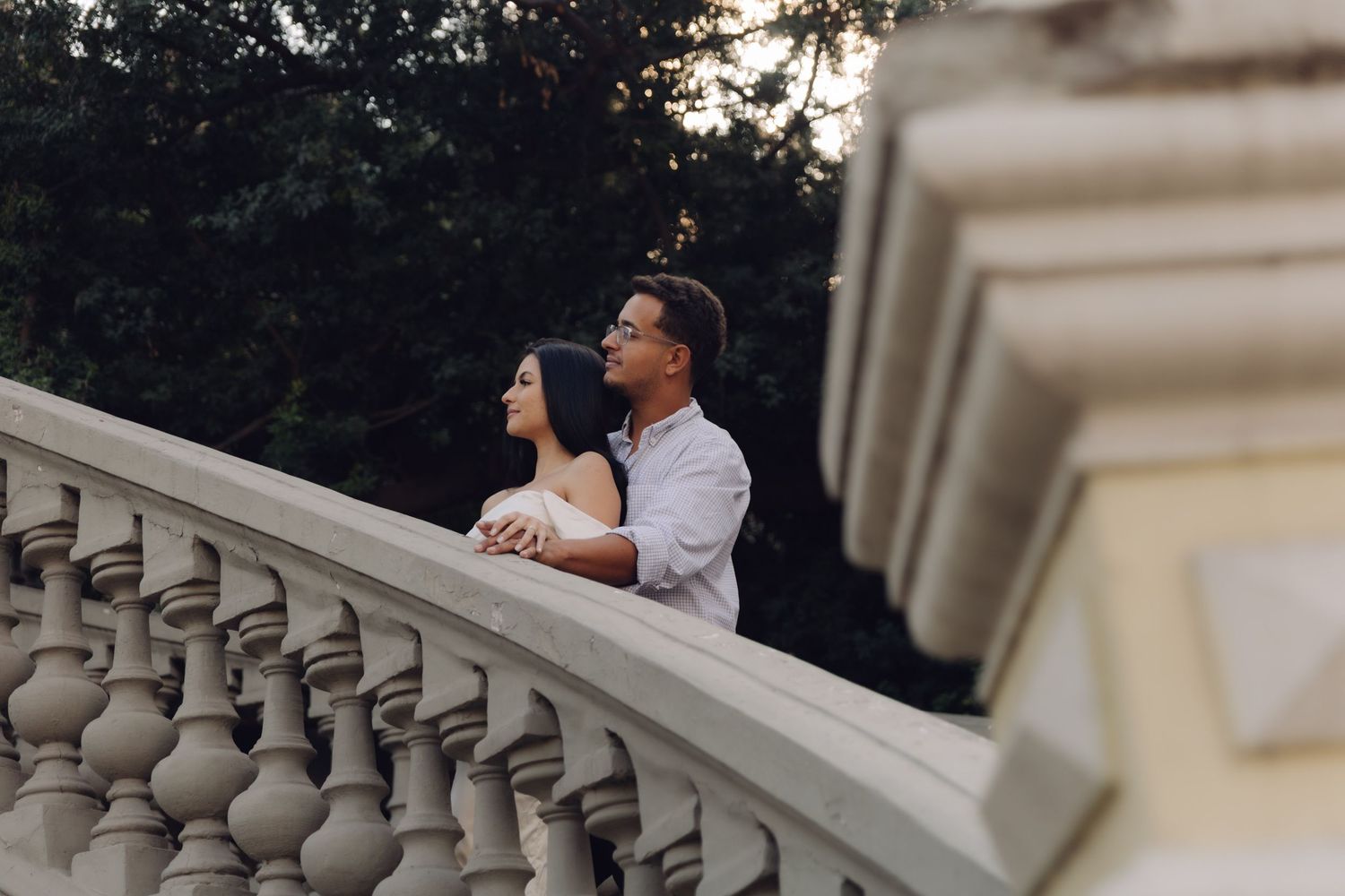 Couple standing close together on a stone balustrade balcony, gazing into the distance peacefully.