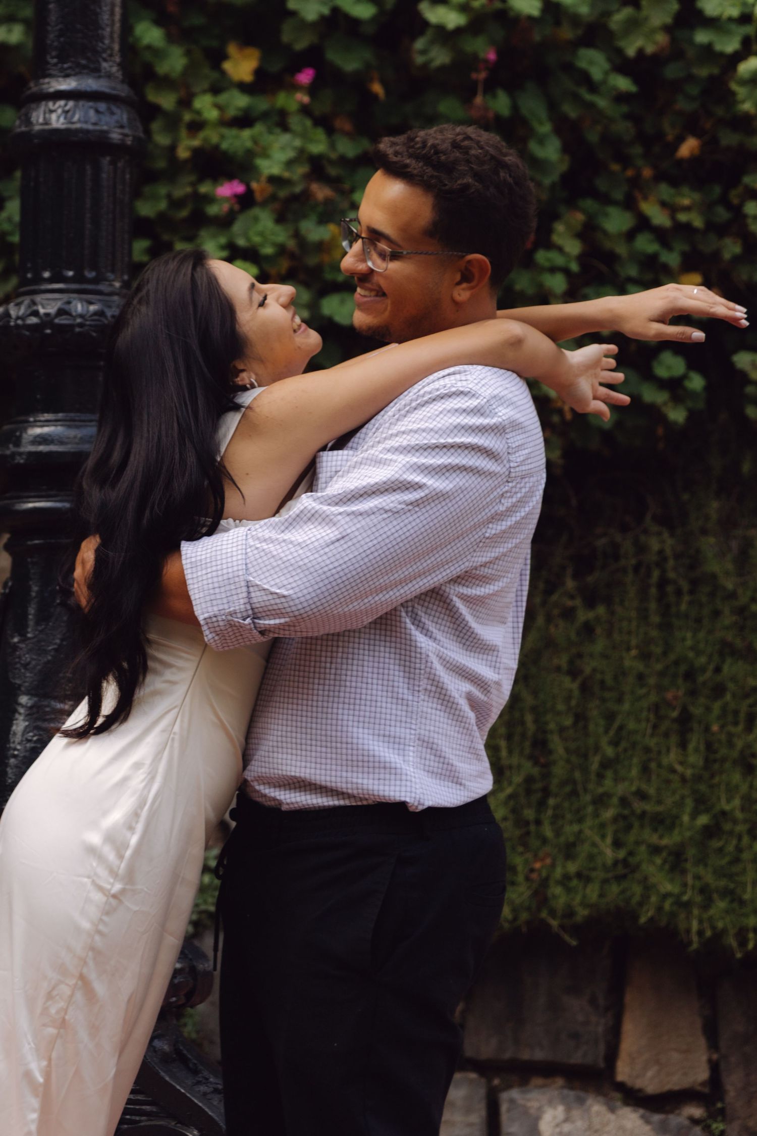 Smiling couple hugging by vintage black lamppost surrounded by lush green ivy wall.