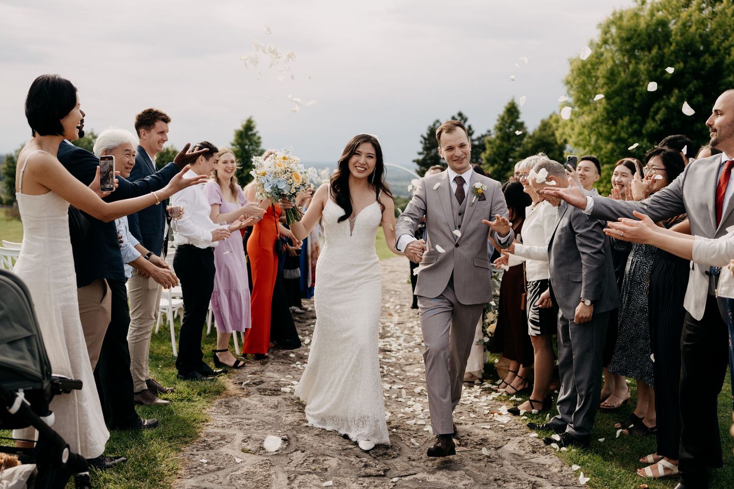 Joyful newlyweds walk through cheering guests tossing confetti during outdoor wedding ceremony exit.