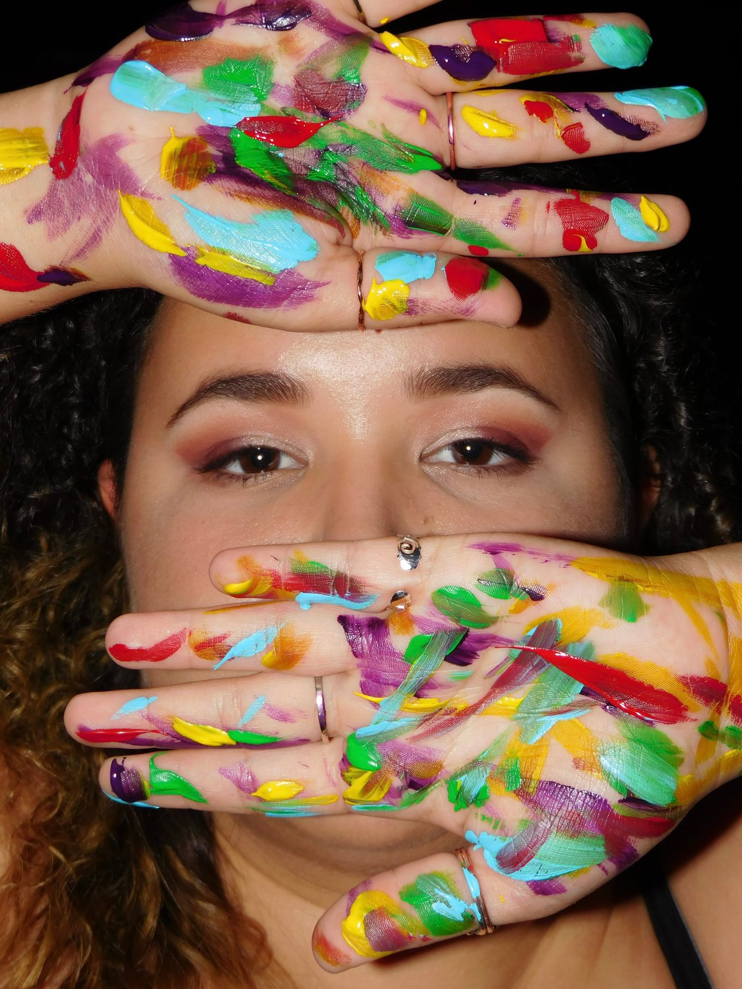 A woman holds up a paint-covered hand toward the camera in a dramatic black and white photo with colorful splashes.