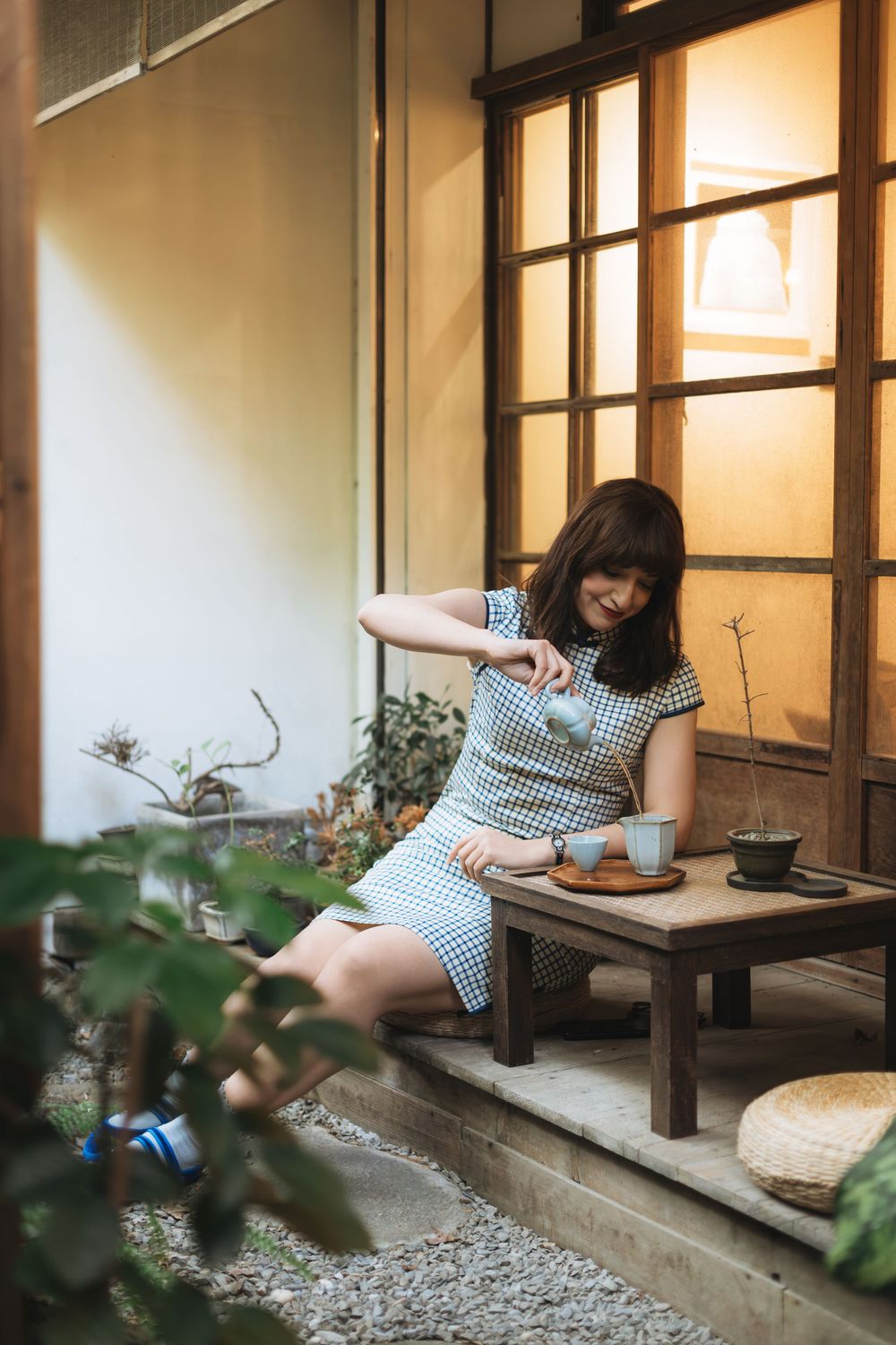 Woman in gingham dress enjoying tea and snacks on a traditional Japanese engawa porch at dusk.