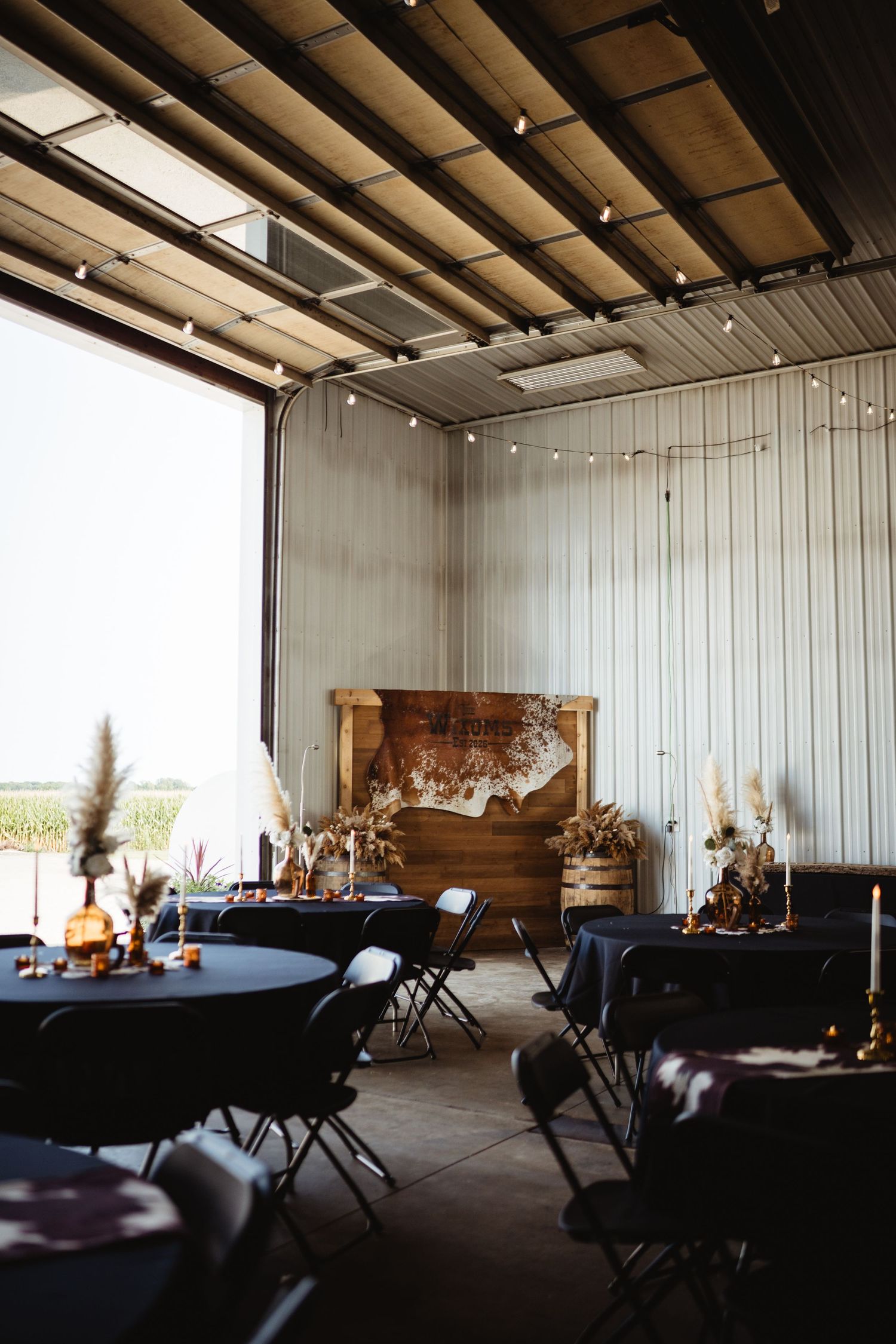 Rustic barn wedding venue with black tablecloths, string lights, and wooden backdrop decor.