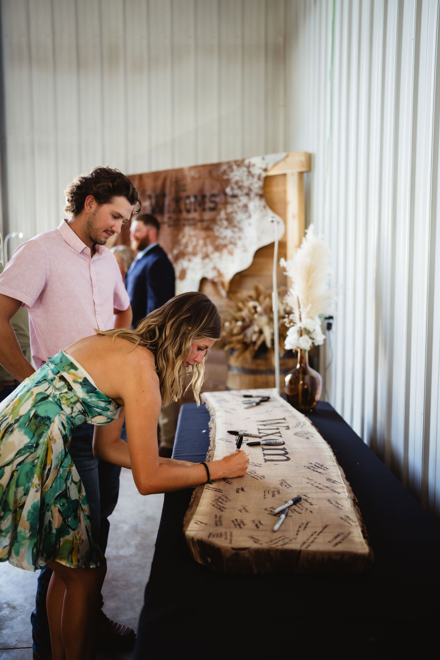 Guests signing a wedding guest book at a decorated table during a reception event.