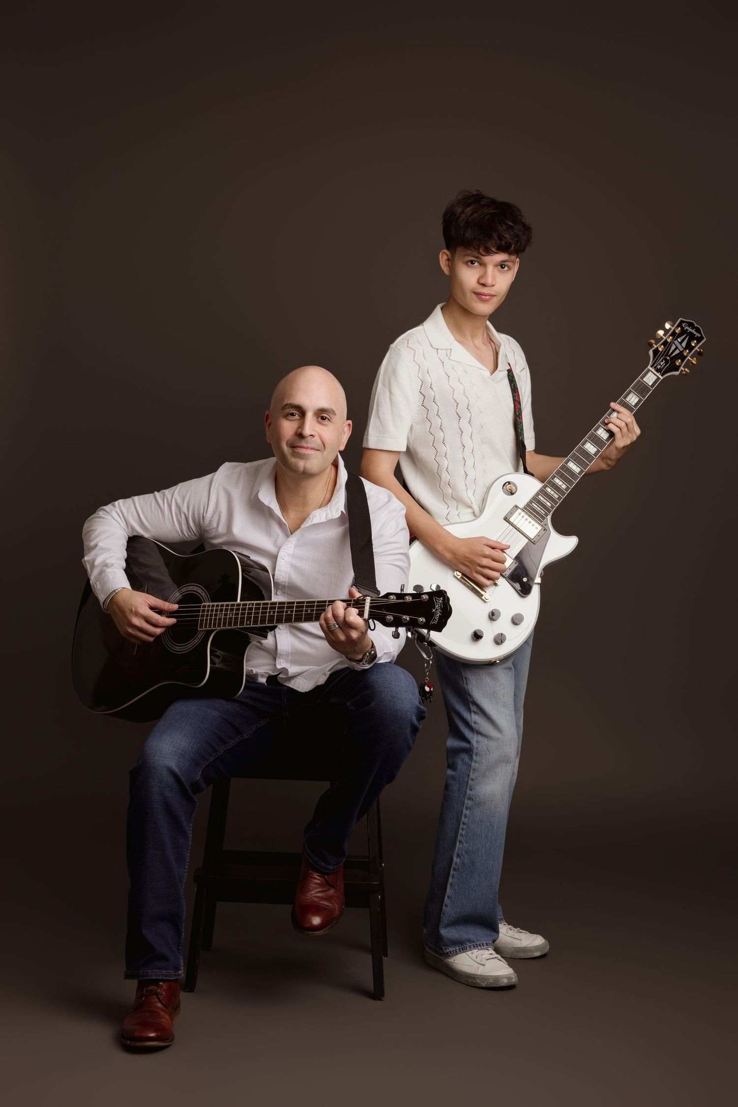 Father and teenage son posing with guitars in a studio