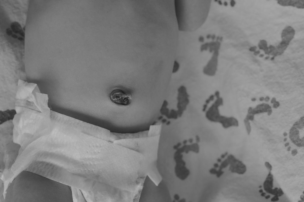 Black and white photo of a newborn baby lying on a blanket with footprint pattern wearing a diaper.