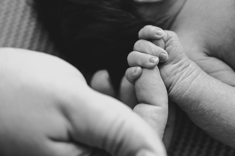 Black and white photo of a newborn baby's tiny hand grasping an adult's finger, symbolizing new life and parental bond.