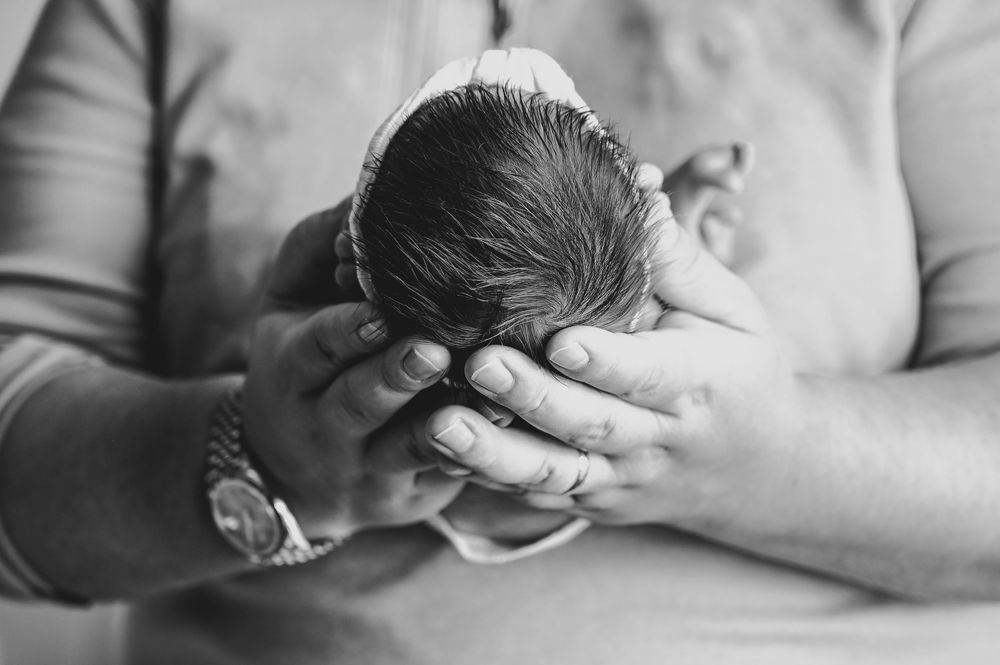 Black and white photo of a newborn baby cradled in loving hands, close-up portrait of infant.