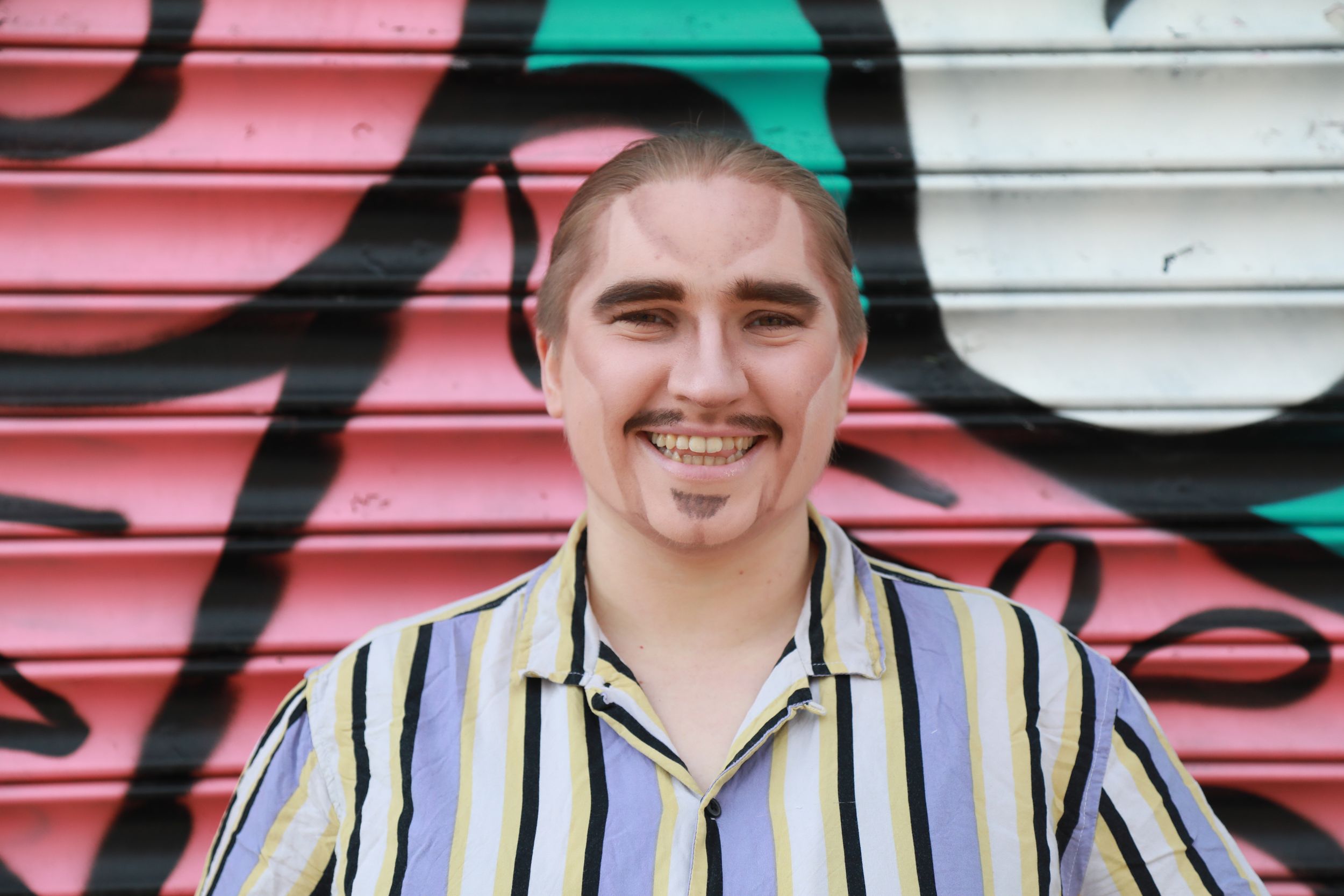 Smiling young person in striped shirt posing in front of colorful graffiti wall.