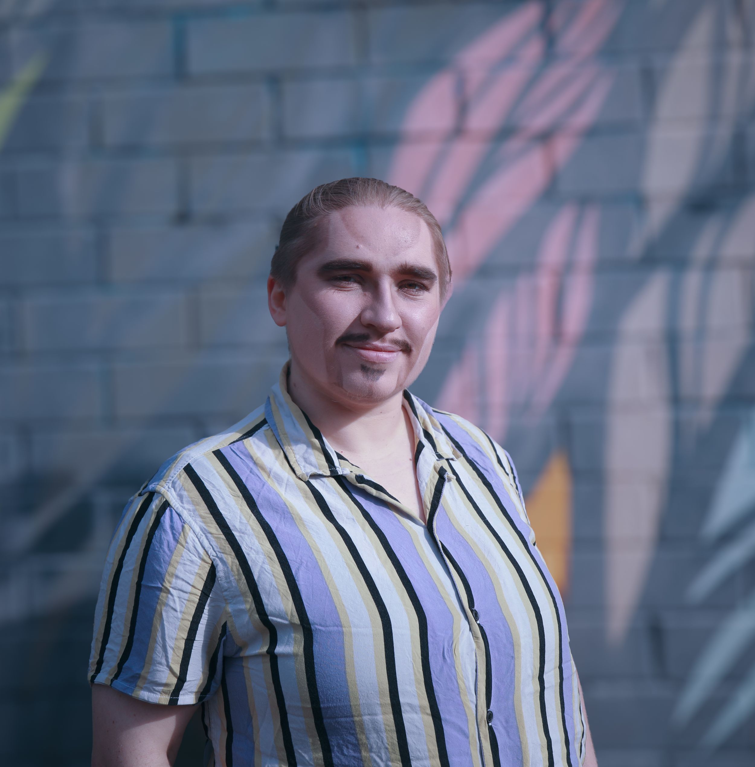 Young person in striped shirt standing before colorful painted mural wall.