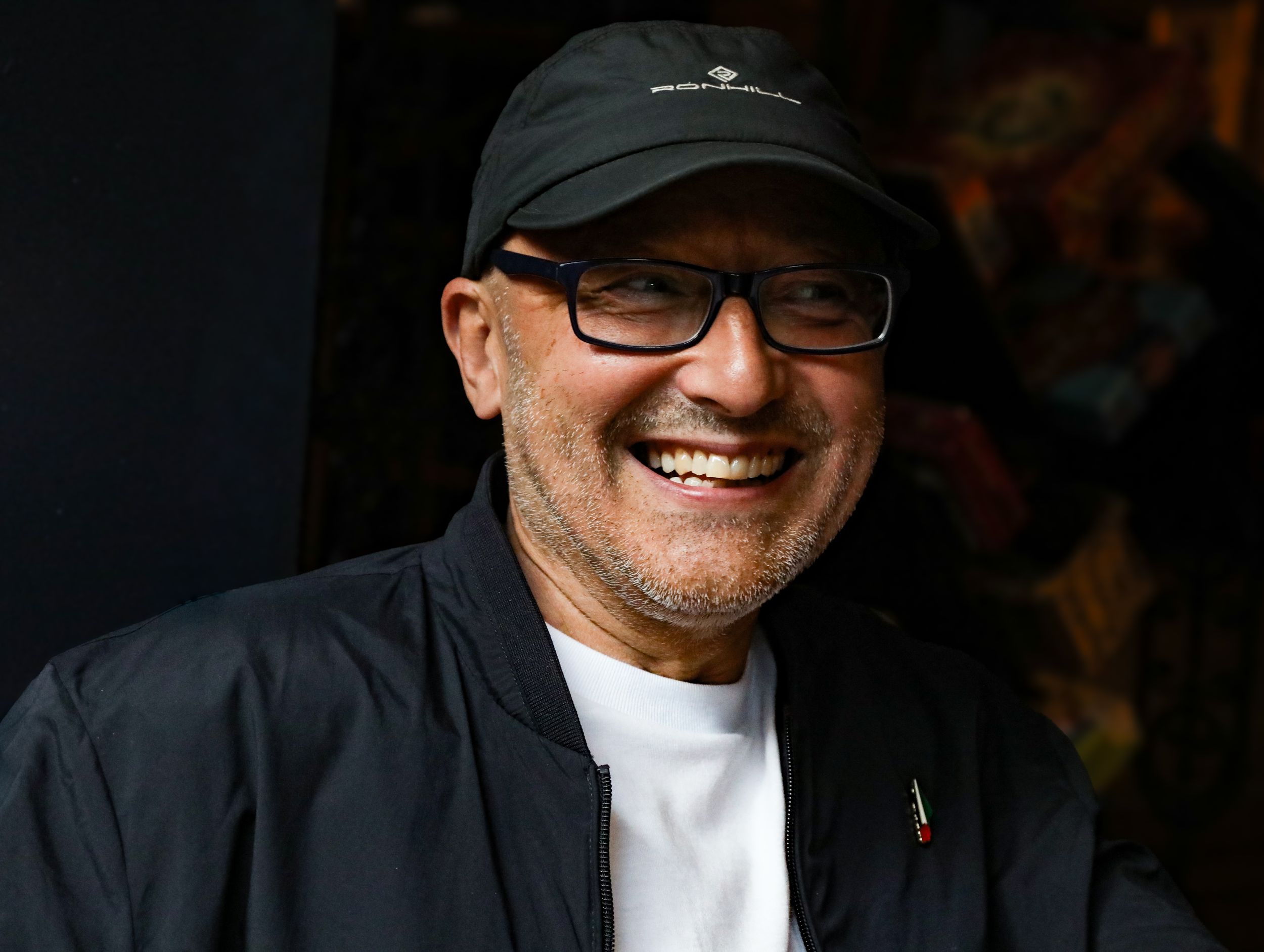 Smiling man wearing black cap and glasses outdoors in candid photo.