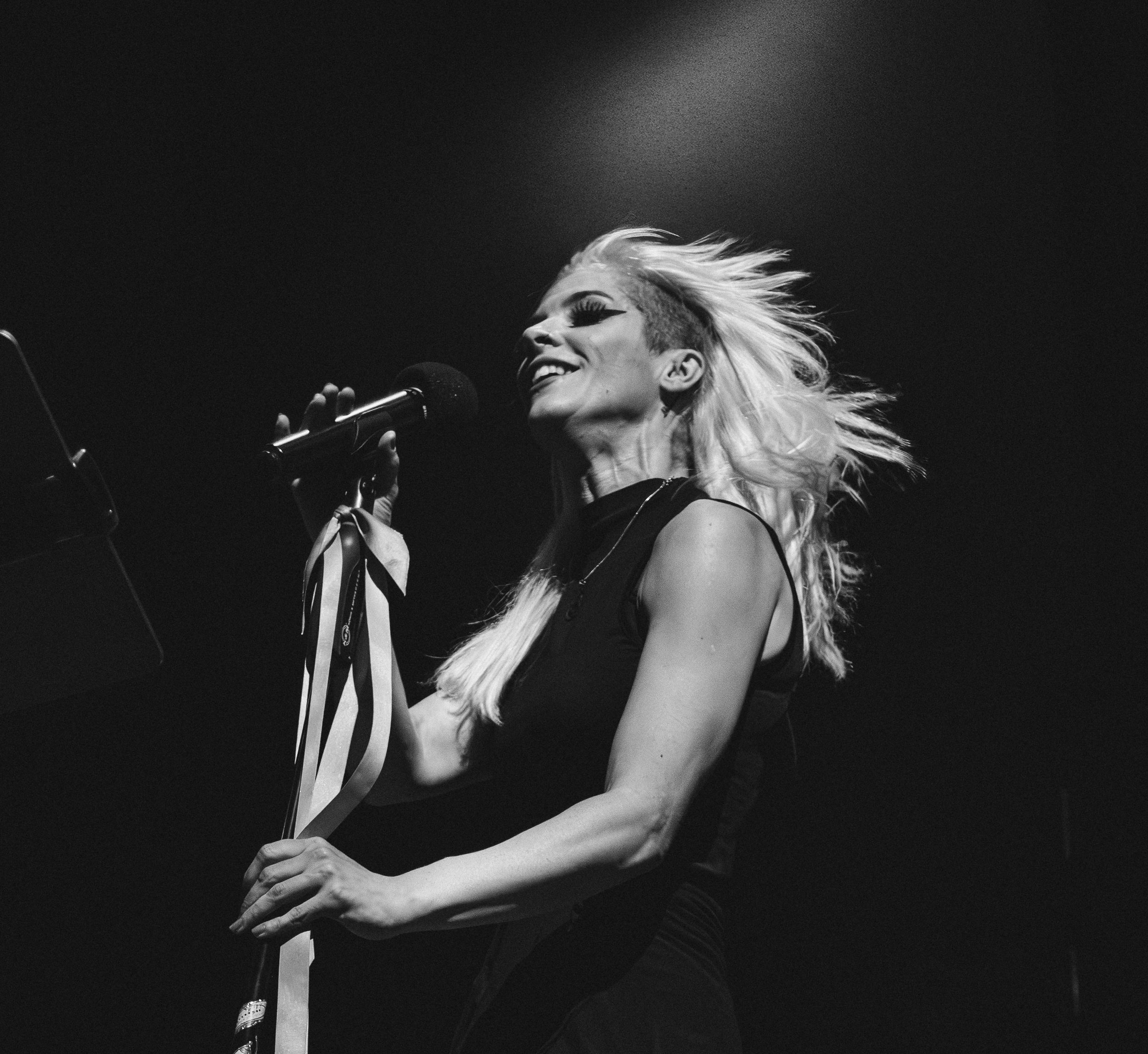 Black and white photo of blonde female singer performing on stage with microphone.
