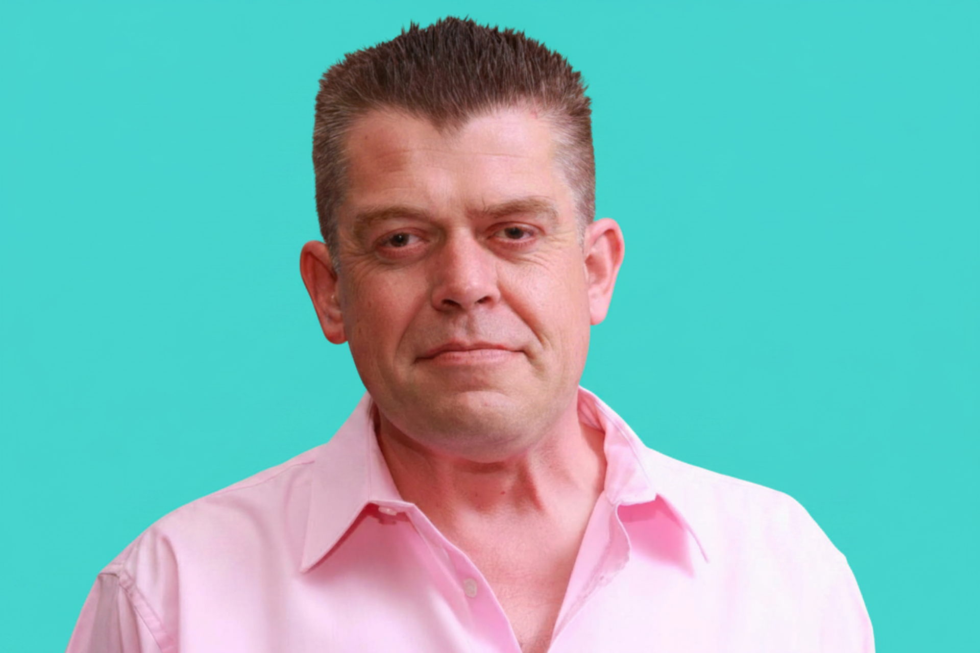 Middle-aged man with short brown hair wearing a pink button-up shirt, smiling against a teal background.