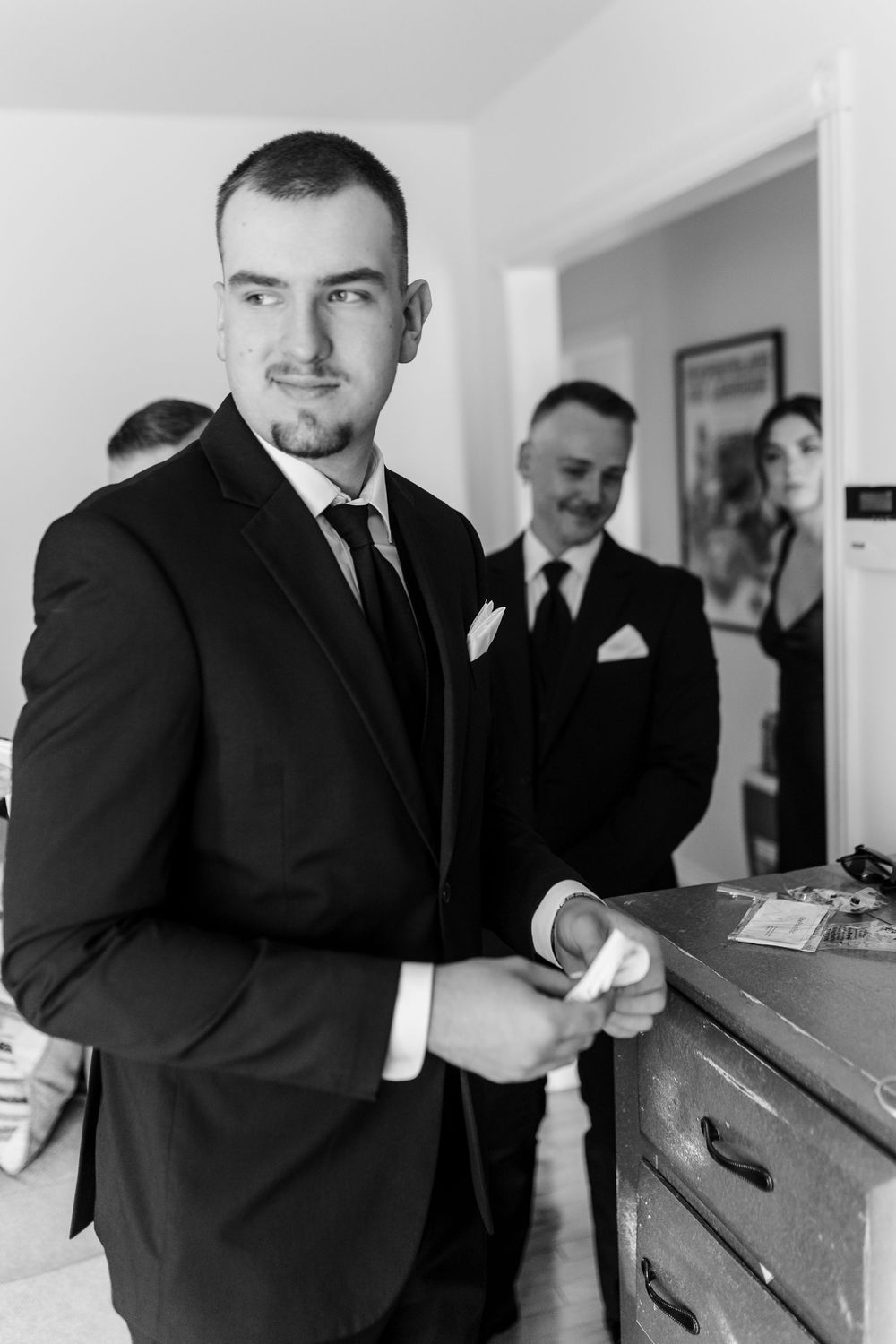 Black and white photo of a groom in a suit adjusting his cufflinks before his wedding ceremony.