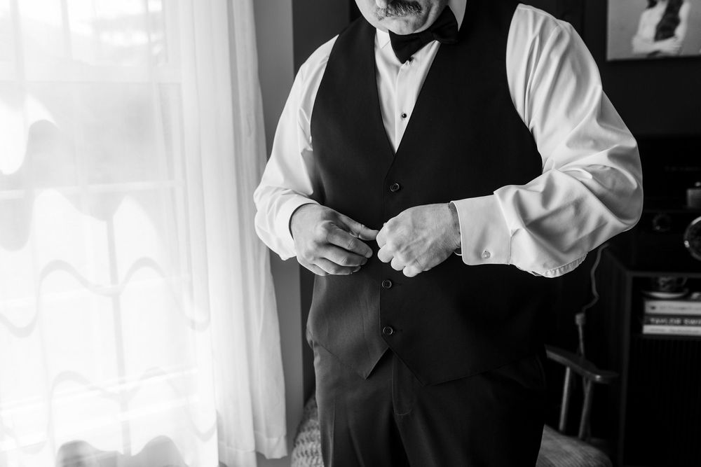 Groom buttoning his vest in black and white photo while getting ready for wedding ceremony.