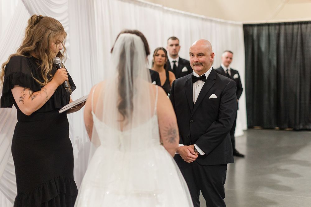 Groom smiling at bride during indoor wedding ceremony while officiant reads vows.