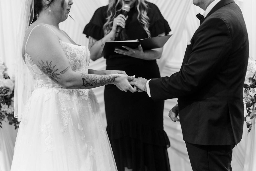Black and white photo of bride and groom exchanging rings with officiant.