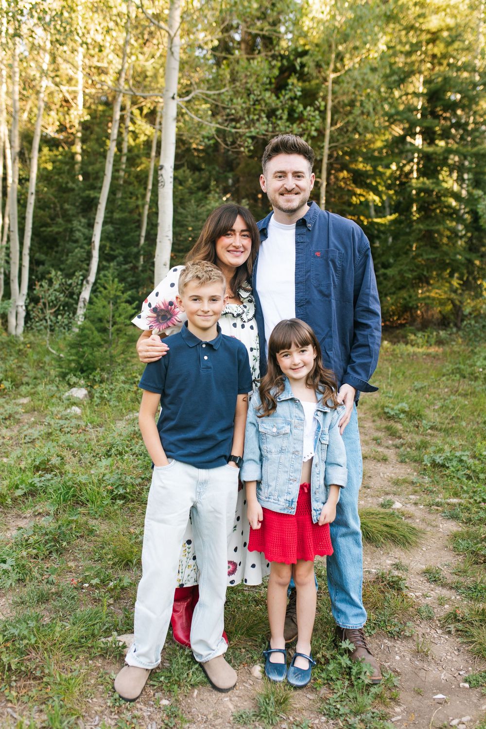 A happy family of four poses outdoors among aspen trees, with two adults and two children smiling together.