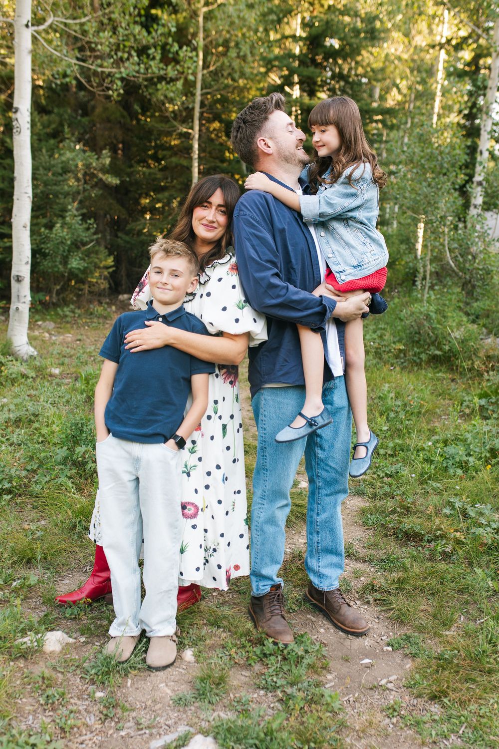 Happy family of four posing outdoors in a forest, parents with two children smiling together on a nature trail.