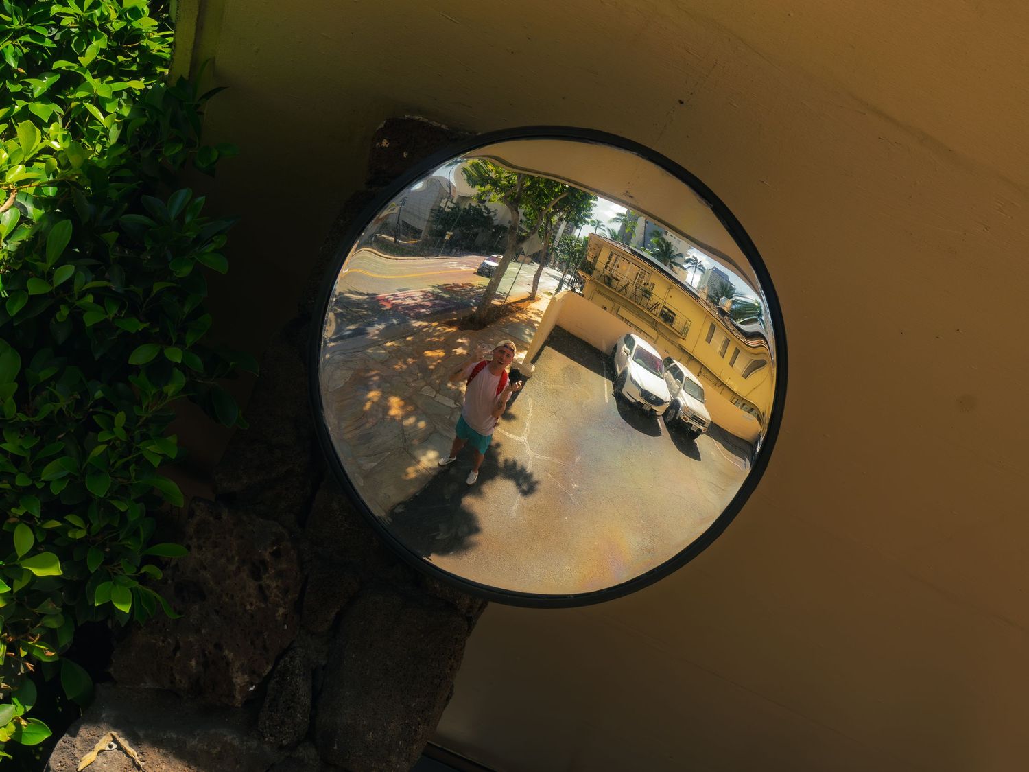 Photographer, Gavin (Bison) Media, reflected in a round convex safety mirror on a sunny street in Waikiki, Hawaii.
