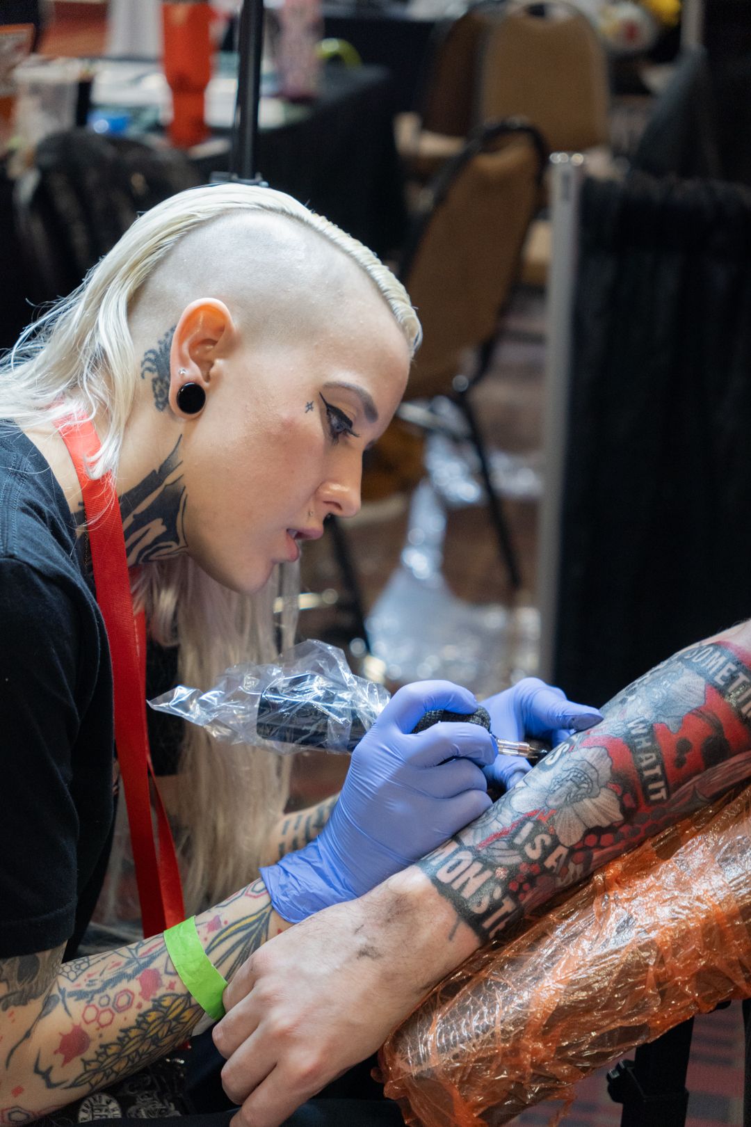 Black and white photo of a tattooed female tattoo artist preparing her equipment at a convention booth.
