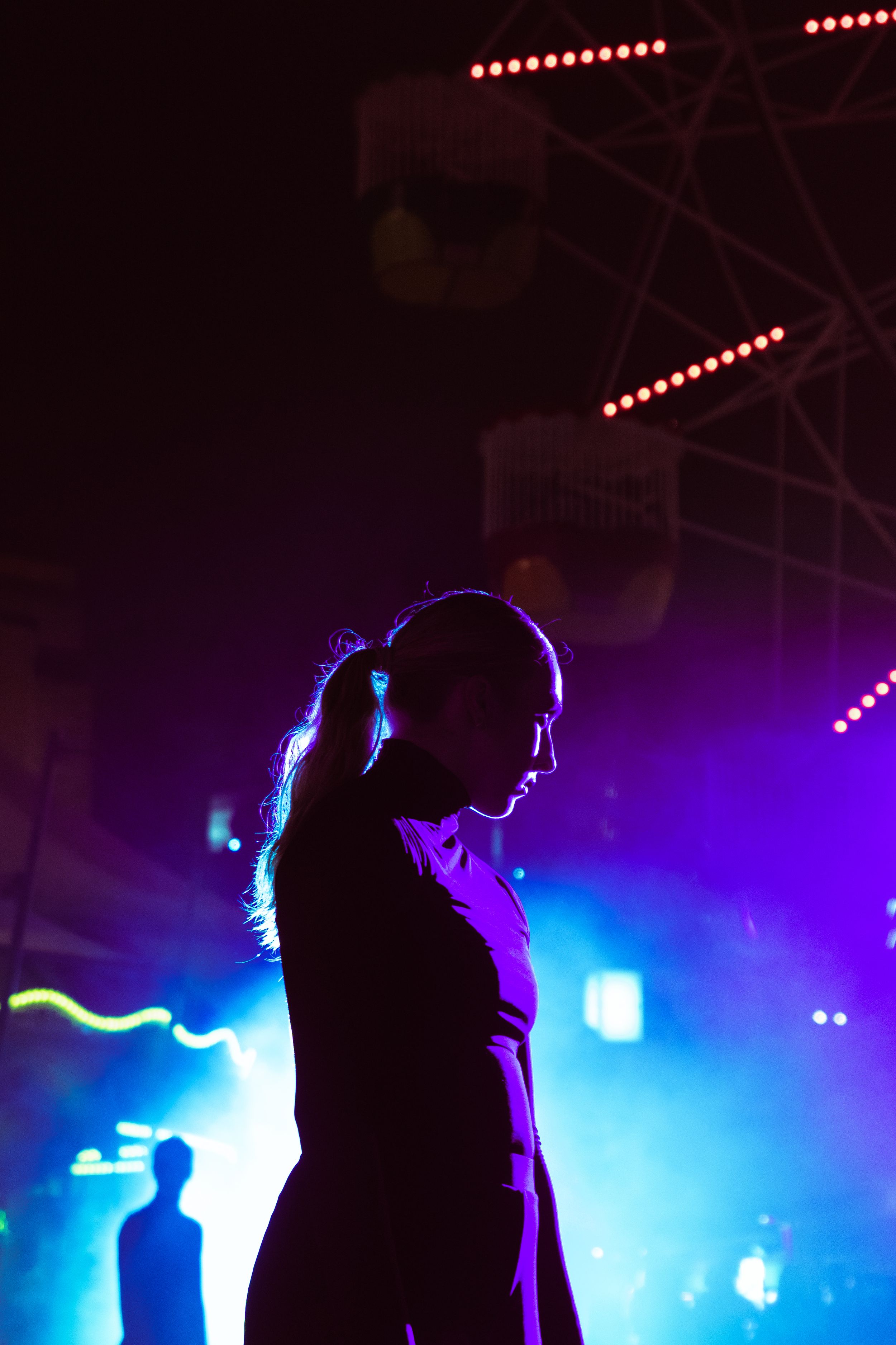 Silhouette of a woman with ponytail at a vibrant concert with blue and purple stage lights.