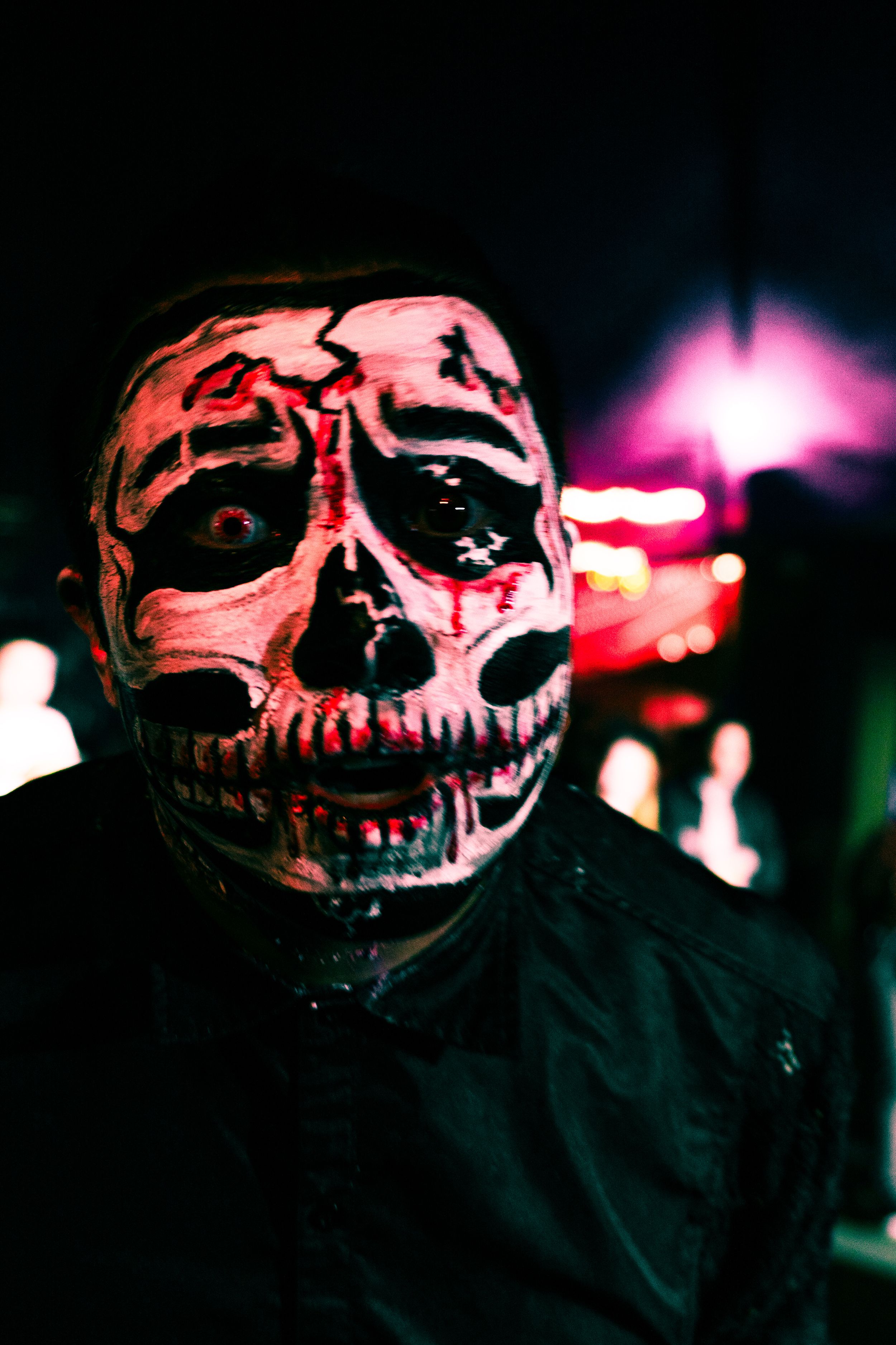 Person wearing terrifying skull zombie mask with red accents at dark Halloween event.