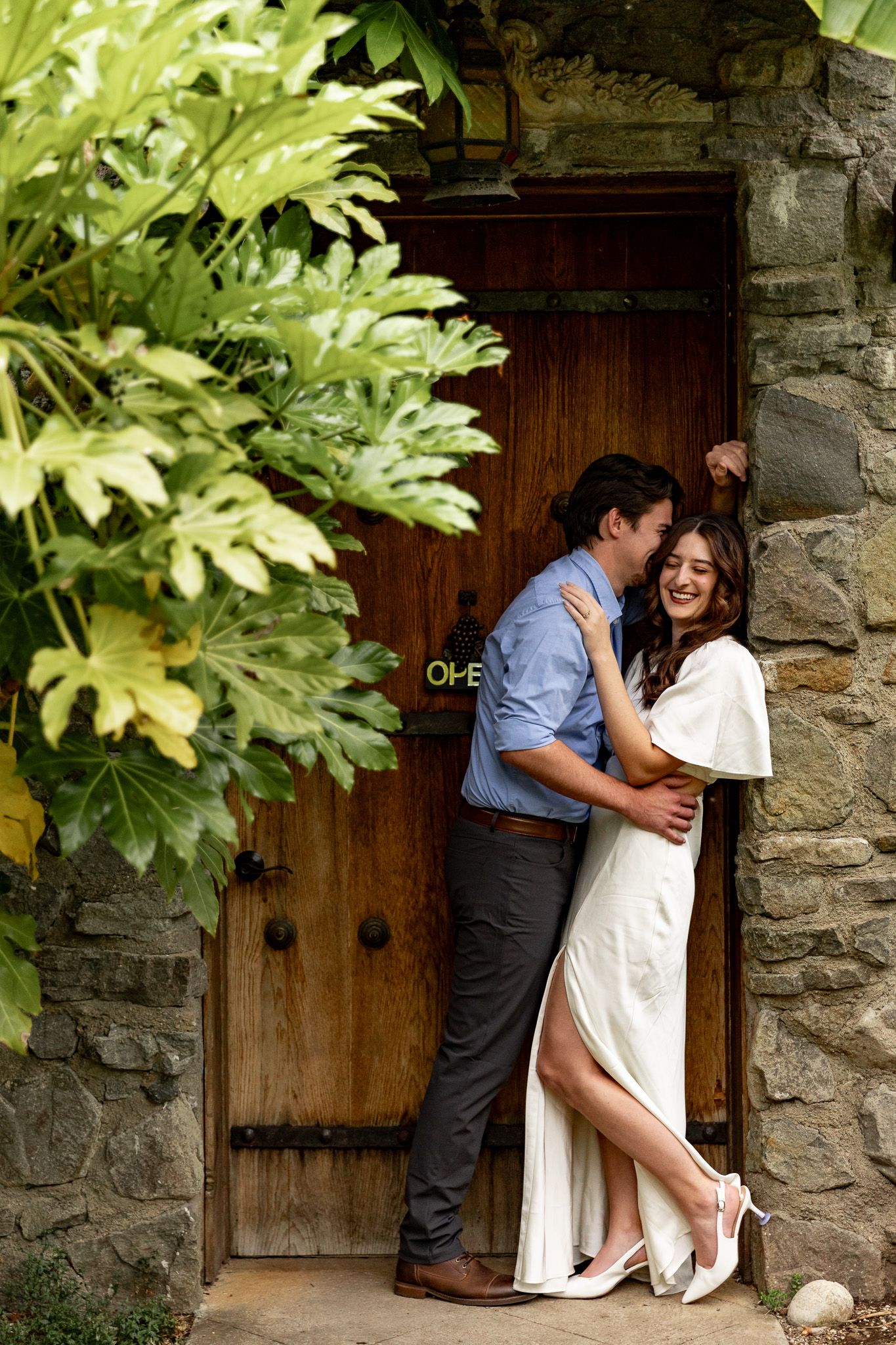 Couple embracing and smiling by a rustic wooden door at Villa Catalana Cellars in Oregon City.