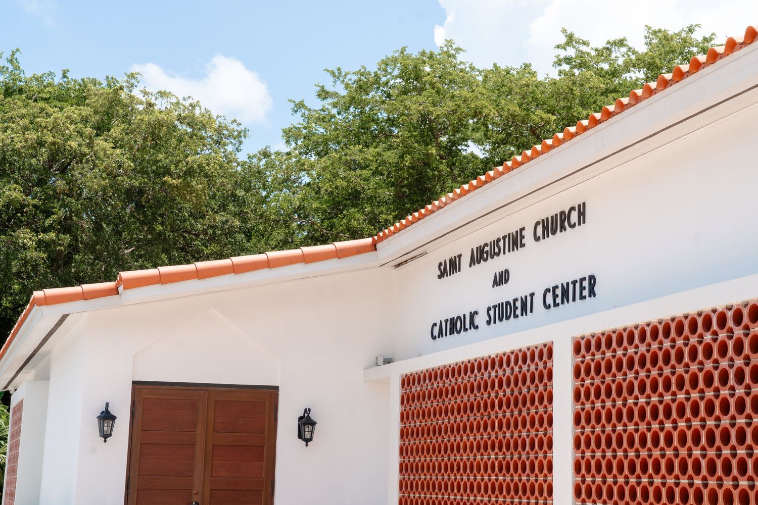 Saint Augustine Church and Catholic Student Center building with white walls, red trim, and lush green trees.