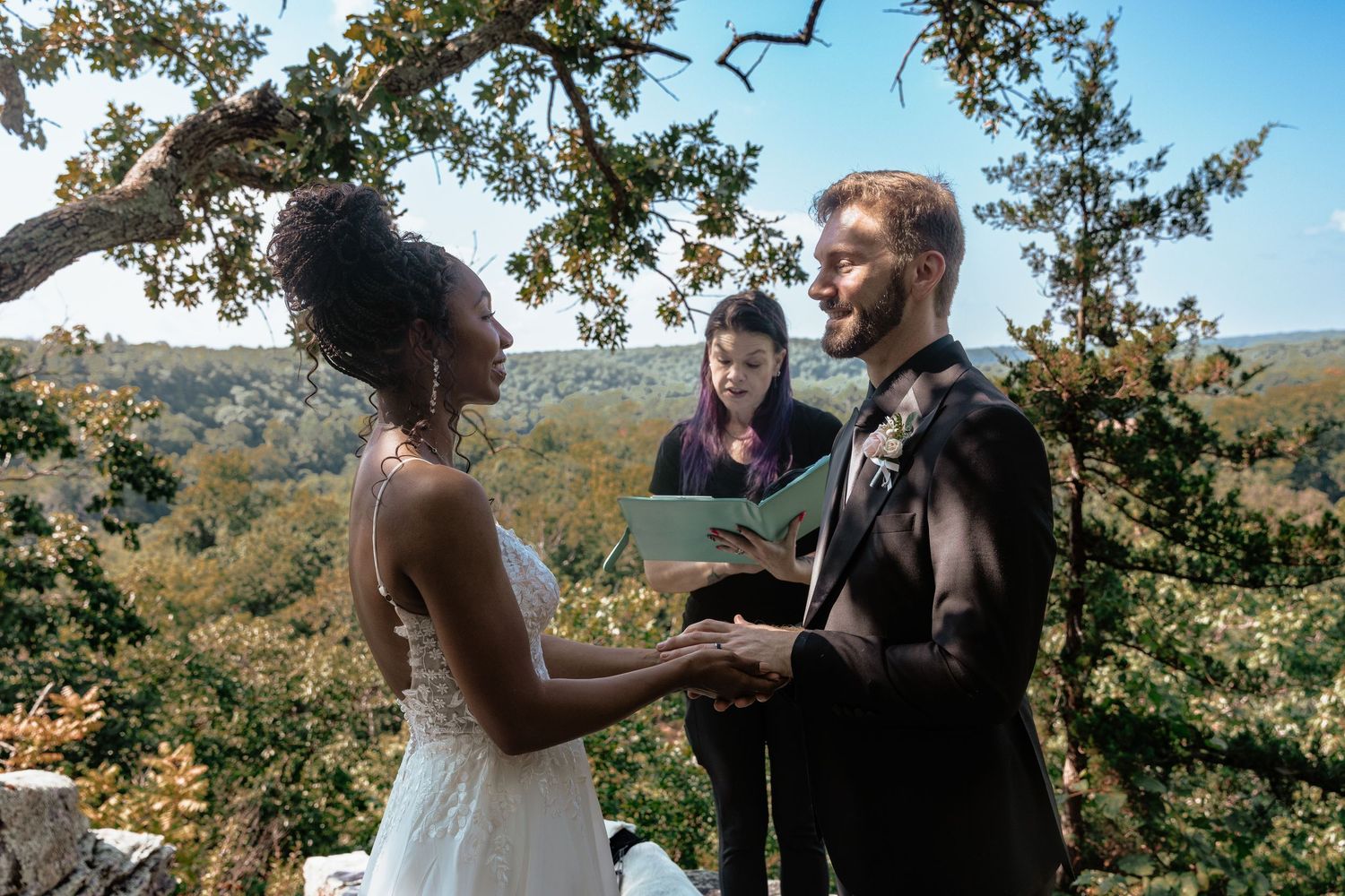 Two people holding small books outdoors, one with red nails and a tattoo, reading during a ceremony.
