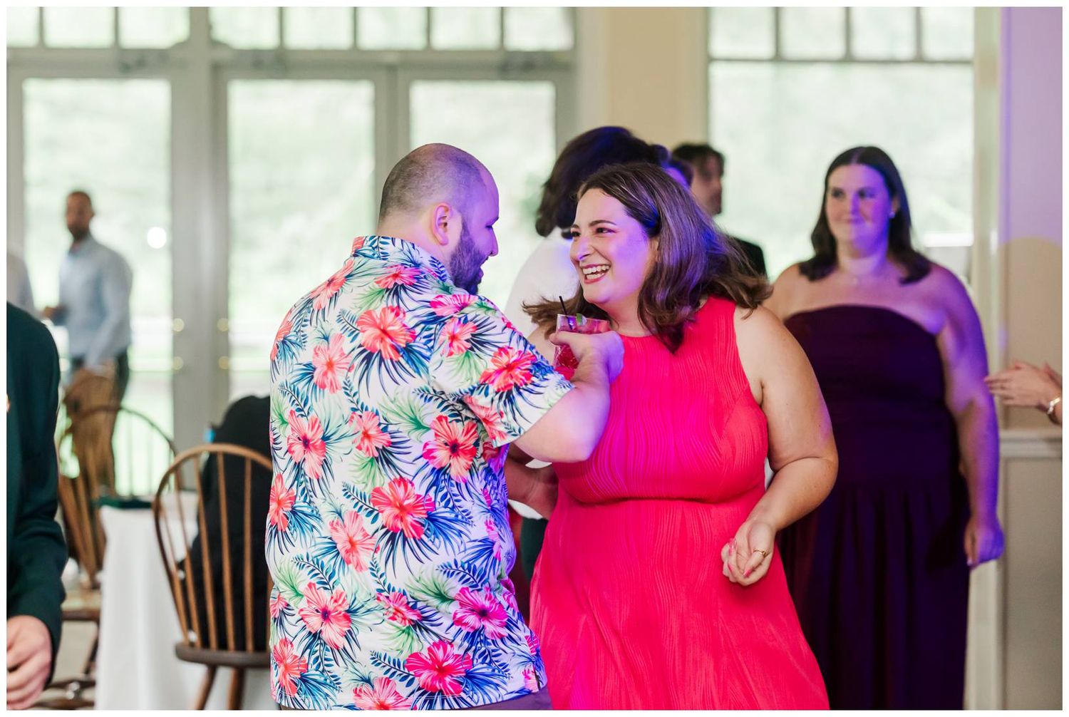 Guests dancing joyfully at a wedding reception, man in floral shirt with woman in red dress.