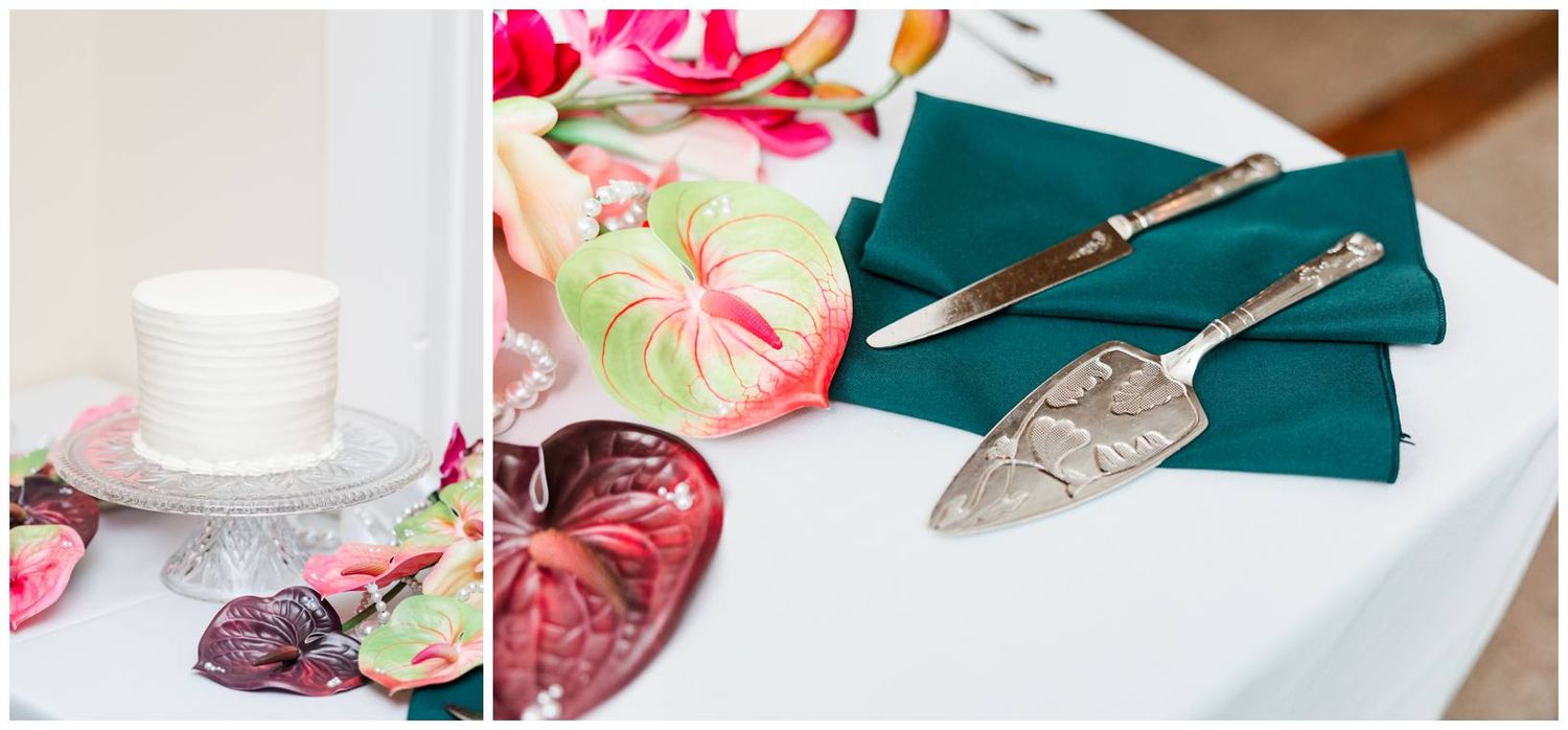 Wedding cake with tropical floral decorations displayed beside elegant silver cake cutting utensils on a teal napkin.