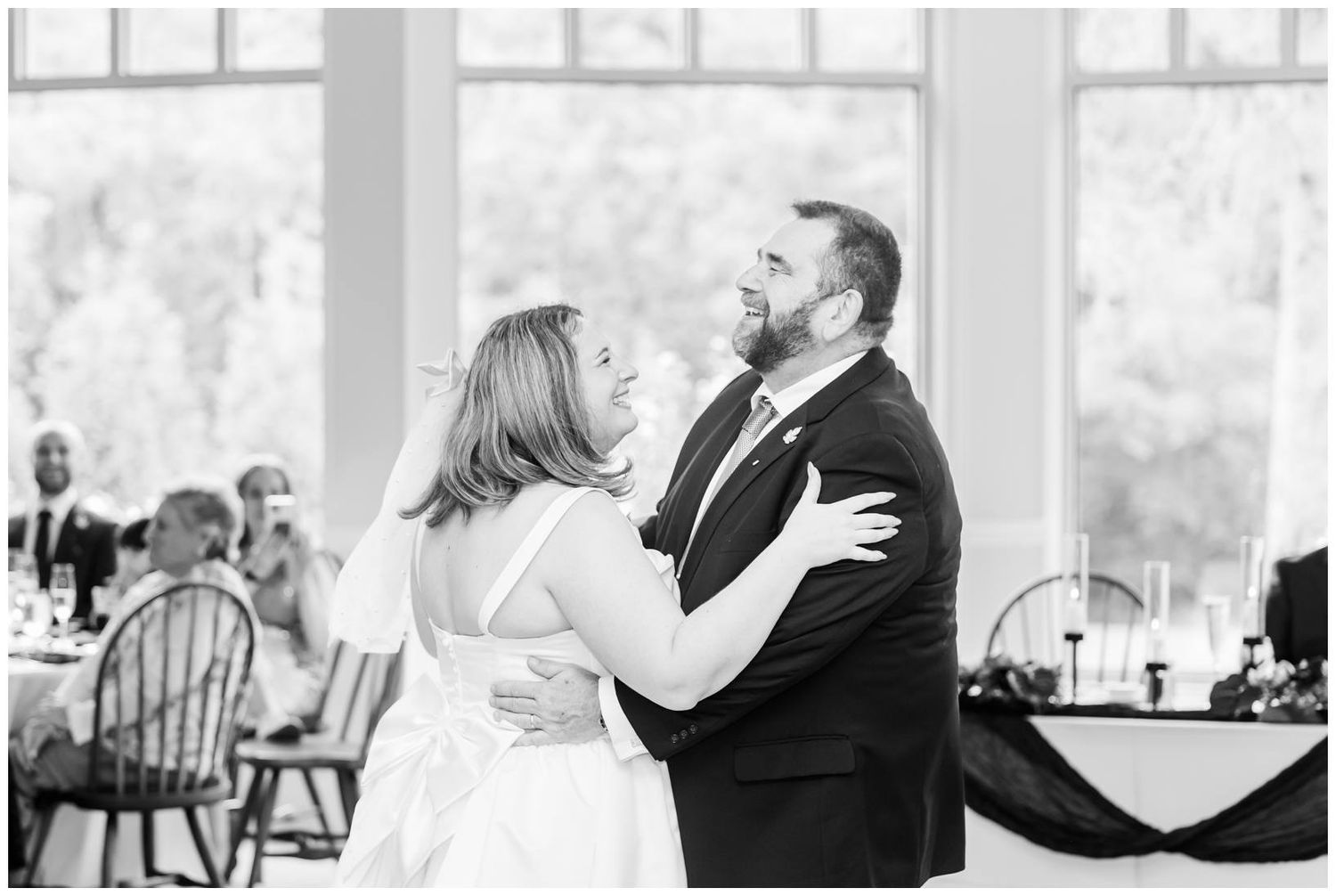 Bride and groom share their first dance in a bright reception hall, captured in elegant black and white photography.