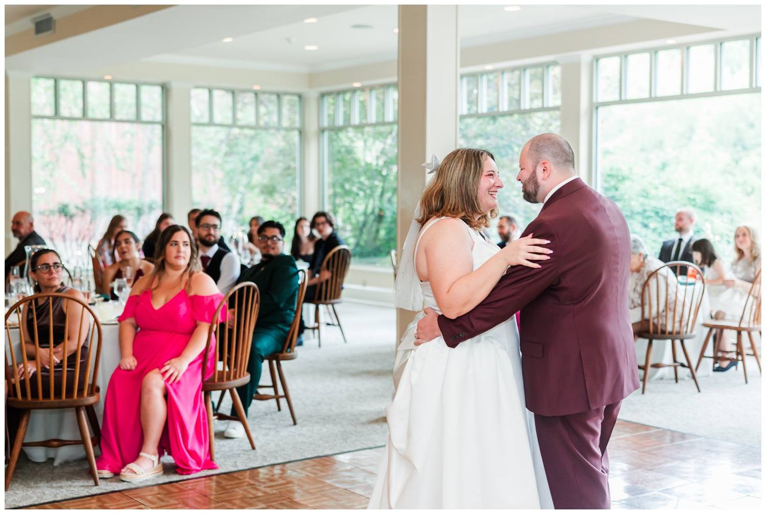 Bride and groom share their first dance while wedding guests watch in a bright, elegant reception venue.