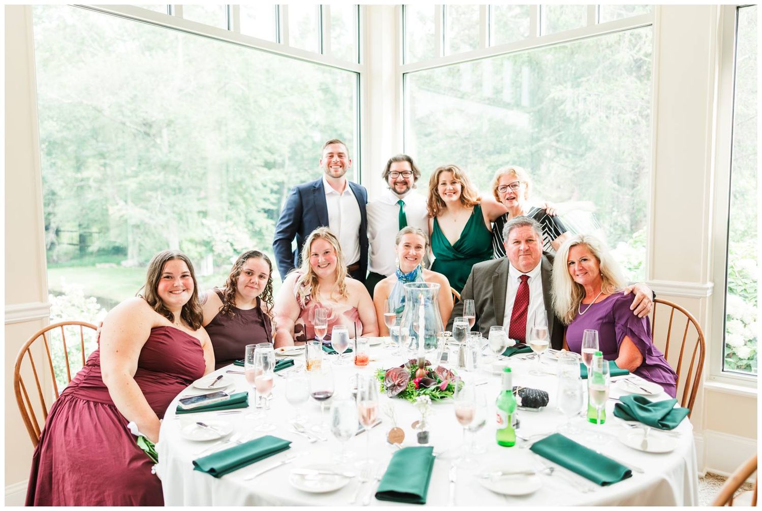 Group of wedding guests smiling at a decorated round table with green napkins during a reception.
