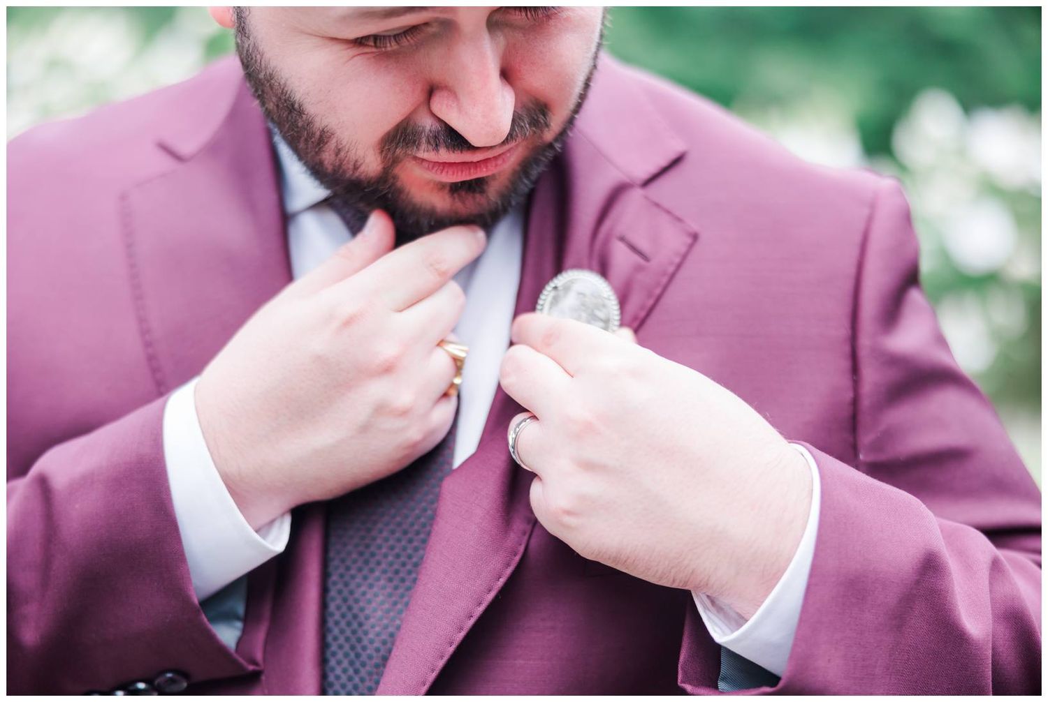 Groom in a burgundy suit fastening his boutonniere before the wedding ceremony.
