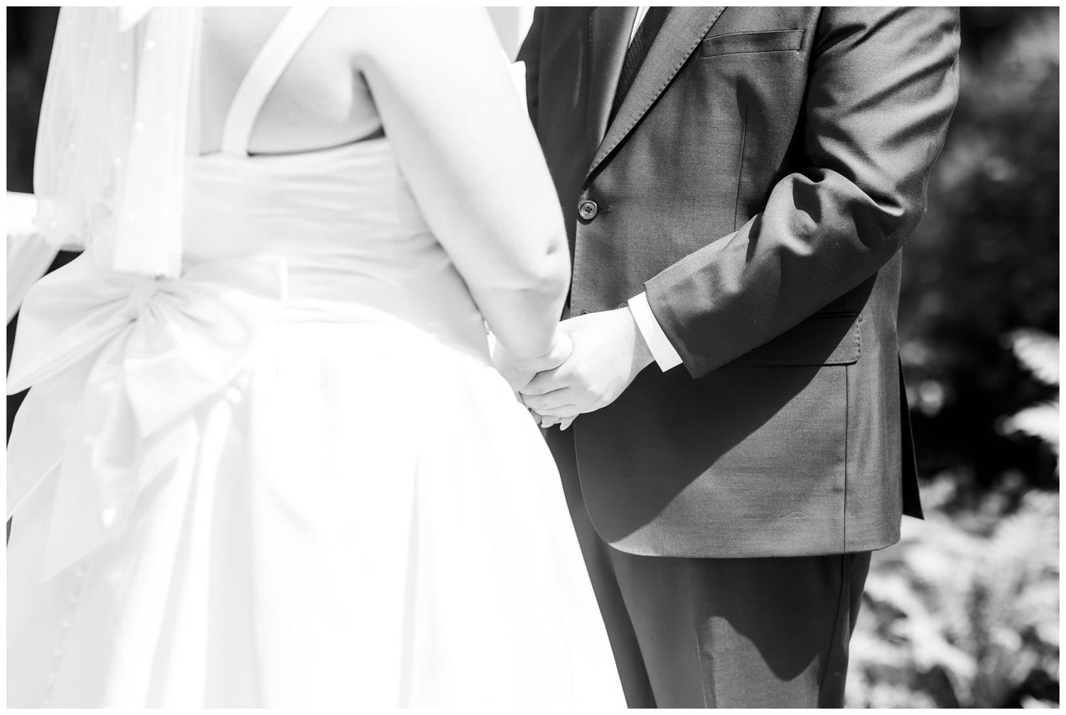 Black and white close-up of bride and groom holding hands at outdoor wedding ceremony.