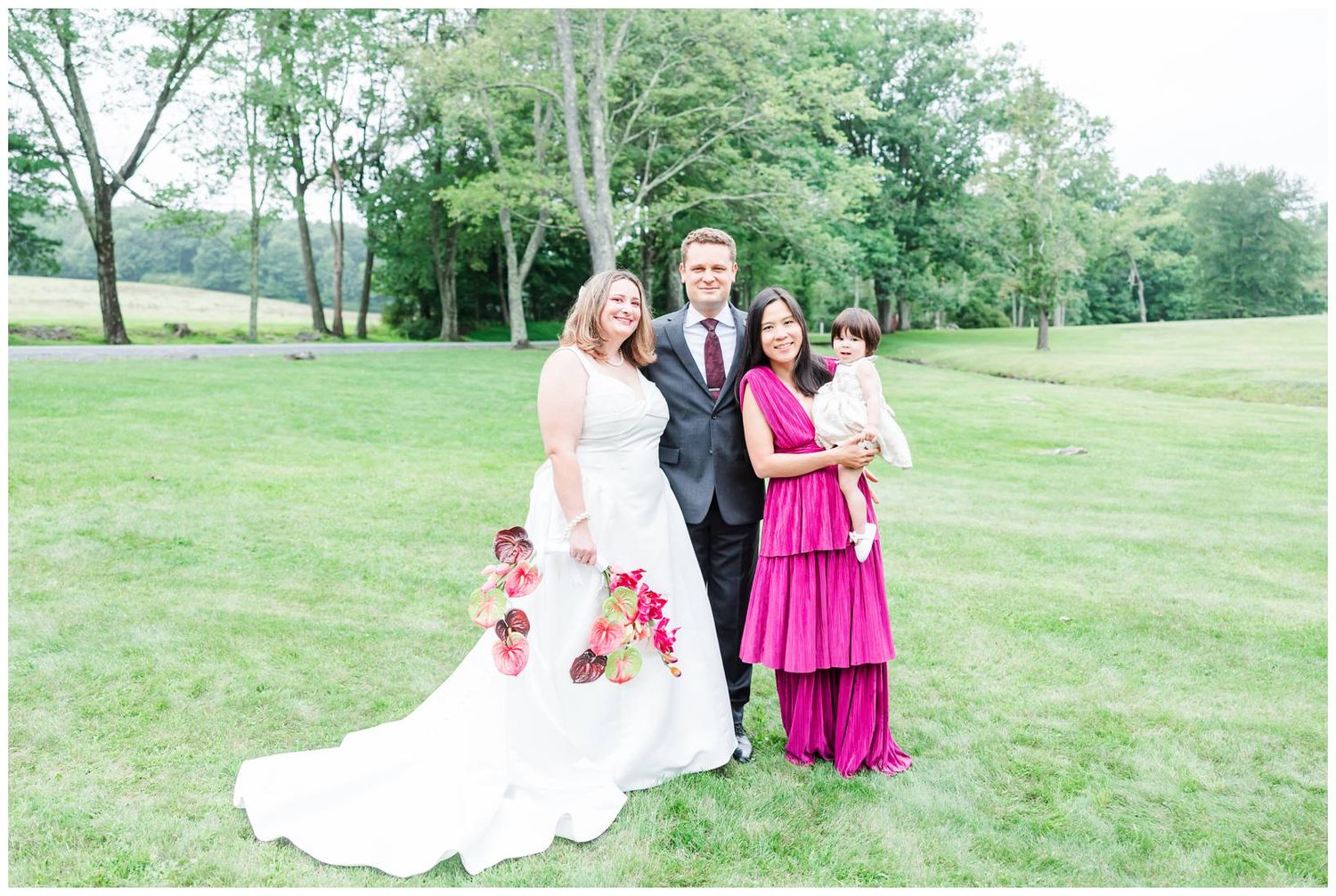 Wedding party poses on lush green lawn with bride in white gown and bridesmaid in fuchsia dress.