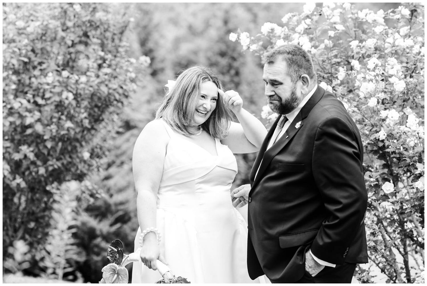 Black and white wedding photo of bride and groom sharing a tender moment outdoors among blooming trees.