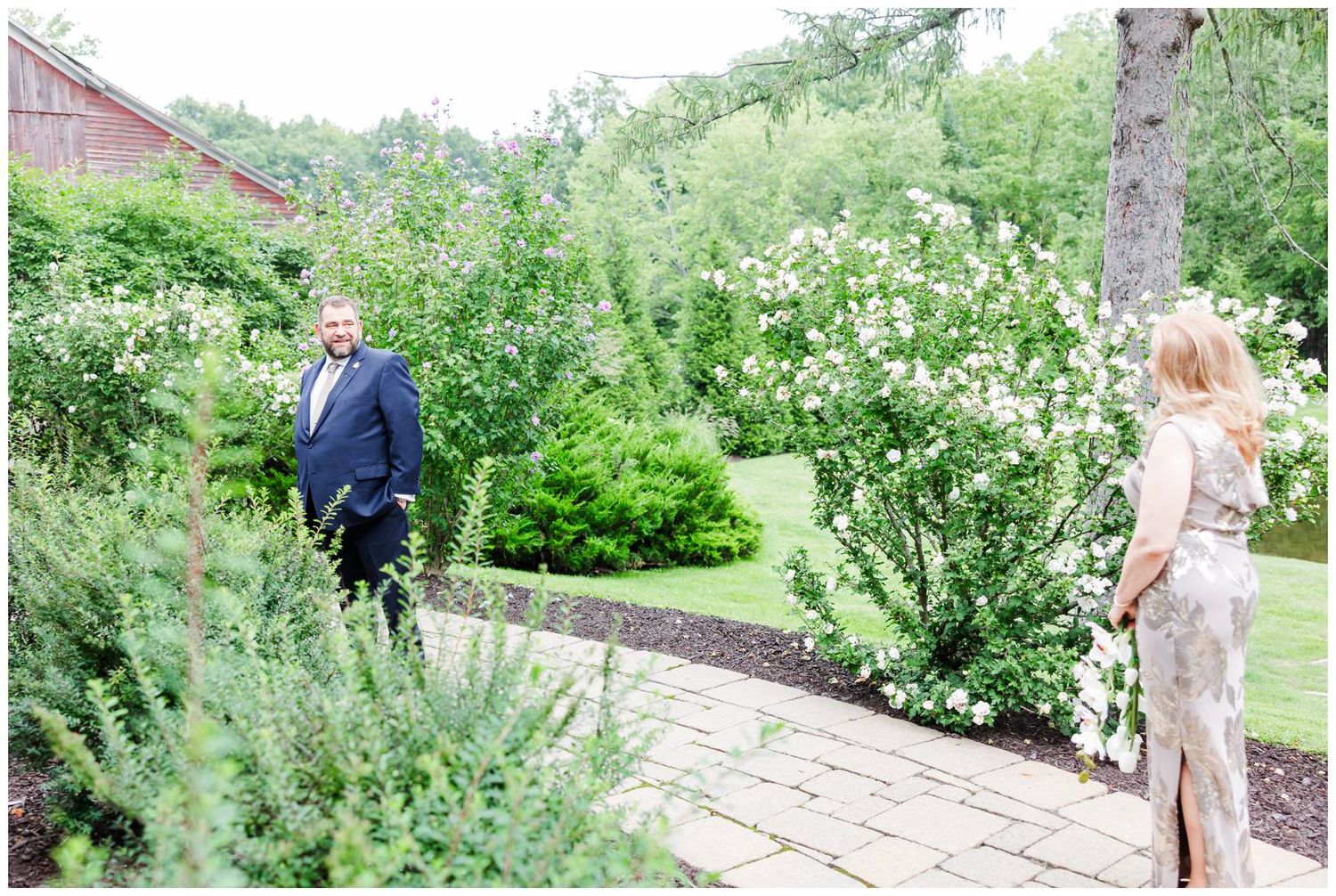Couple sharing a first look moment in a lush garden with white flowering bushes.